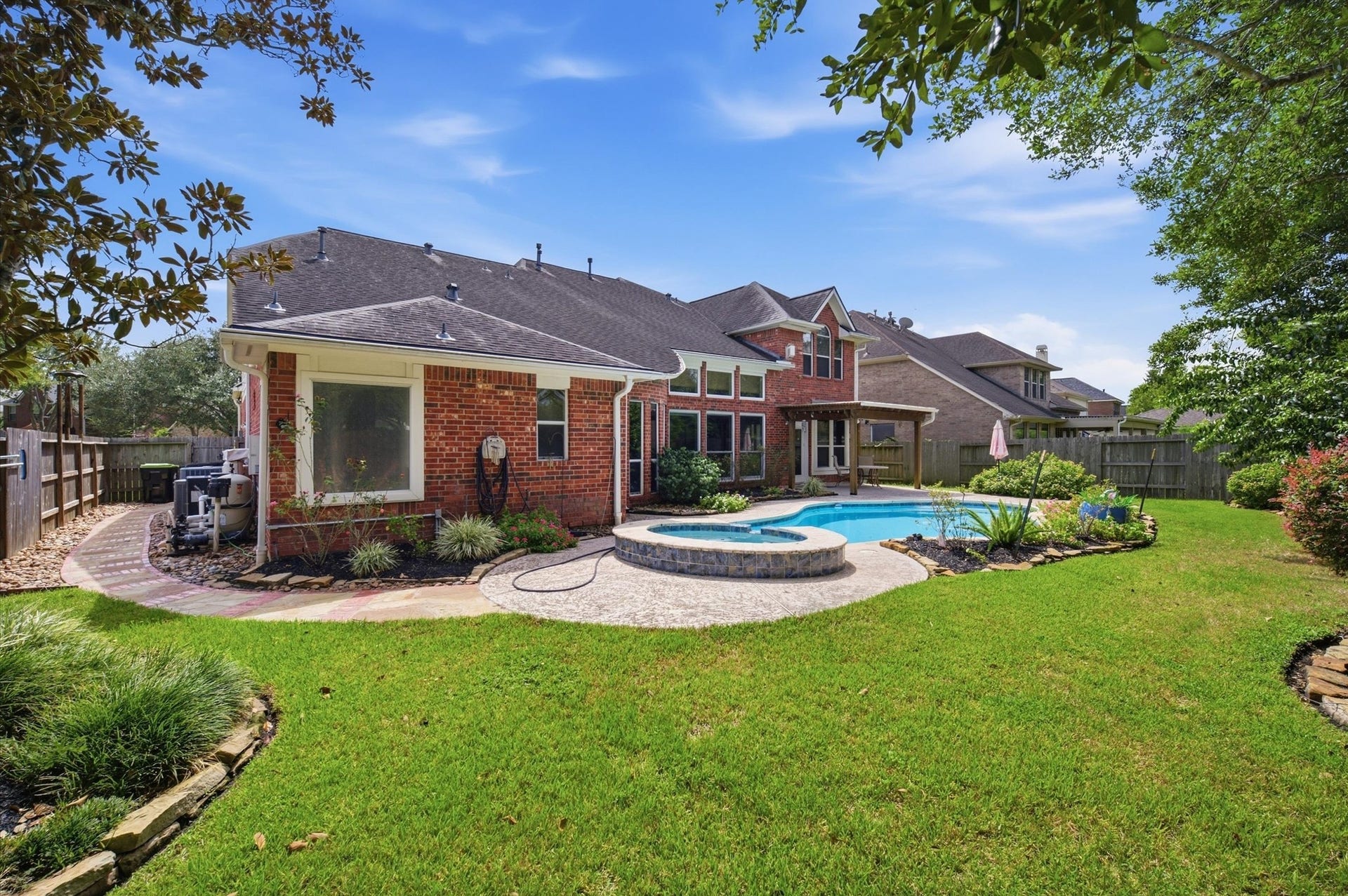 4427 Shady River, Missouri City, TX 77459 Charming brick home with a spacious backyard featuring a pristine pool and hot tub, surrounded by lush greenery and a well-maintained lawn.
