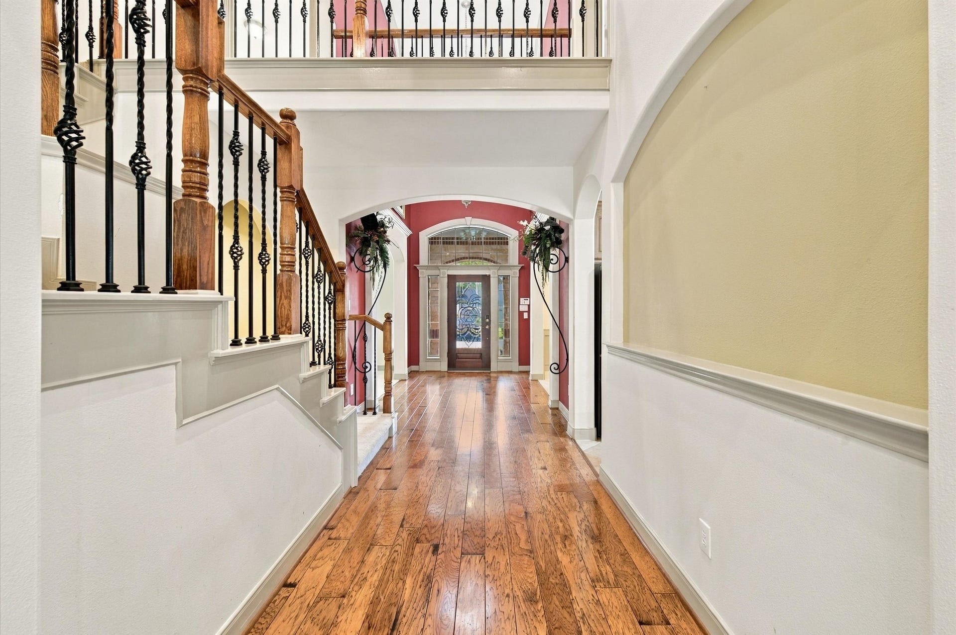 4427 Shady River, Missouri City, TX 77459 Elegant hallway with rich hardwood floors, decorative iron railings, and an inviting arched entryway leading to a glass-paneled front door.