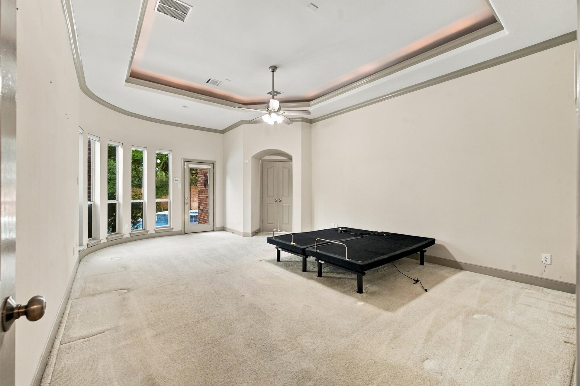4427 Shady River, Missouri City, TX 77459 Spacious bedroom with elegant tray ceiling, abundant natural light from large windows, and direct access to the outdoor pool area for seamless indoor-outdoor living.