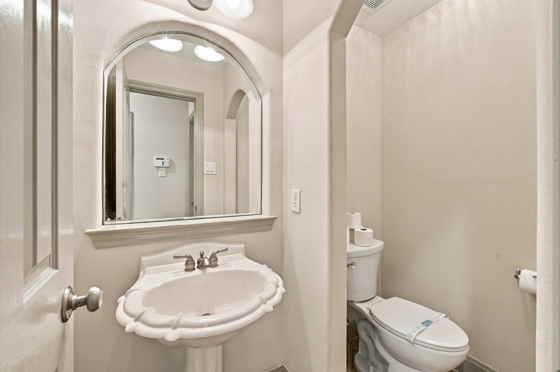 4427 Shady River, Missouri City, TX 77459 Charming powder room featuring a classic pedestal sink and elegant arched mirror, offering a cozy and inviting atmosphere.