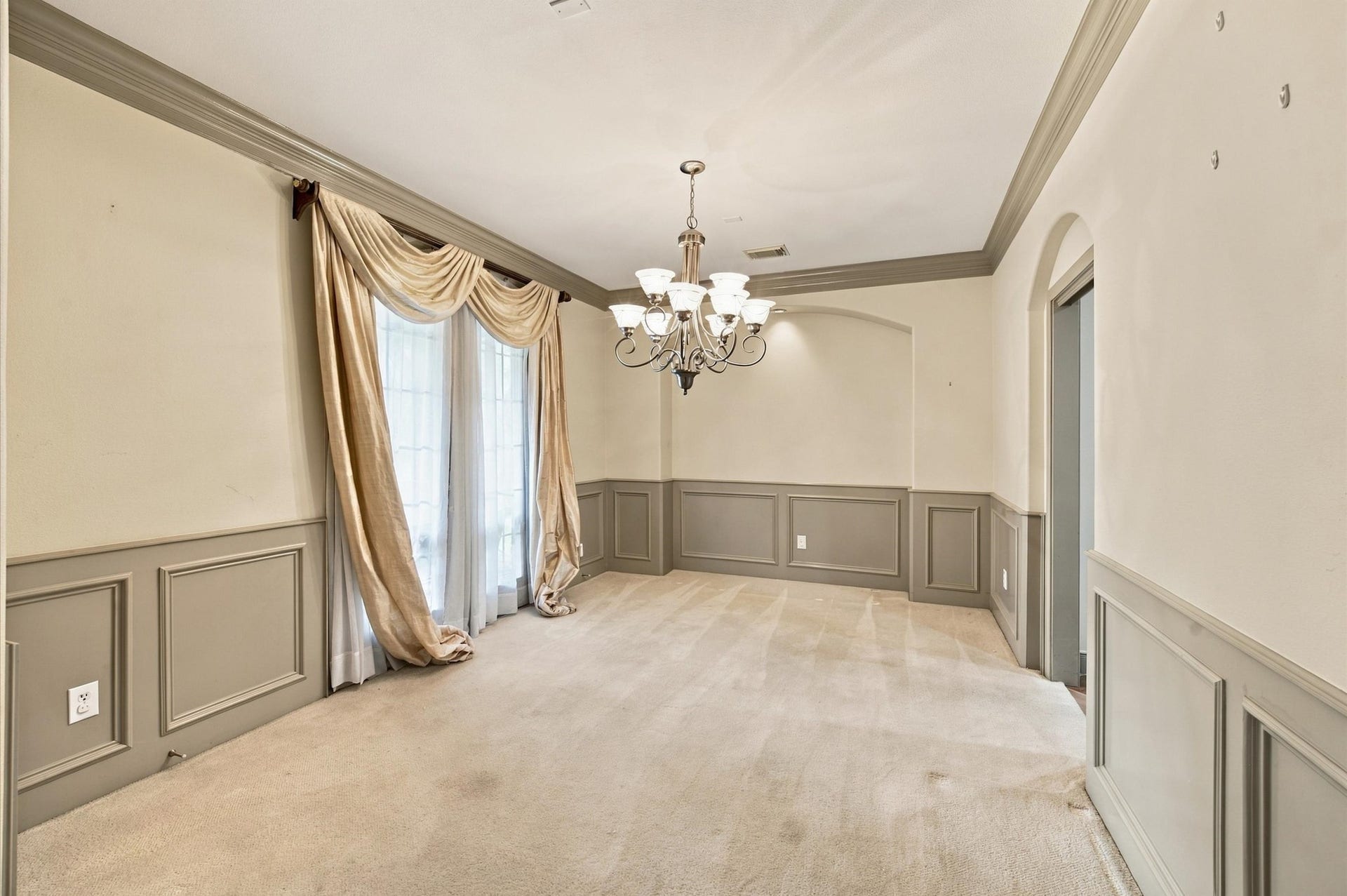 4427 Shady River, Missouri City, TX 77459 Elegant dining room featuring soft carpeting, classic wainscoting, and a stylish chandelier. Natural light filters through the large windows adorned with luxurious drapes, creating a warm and inviting atmosphere.