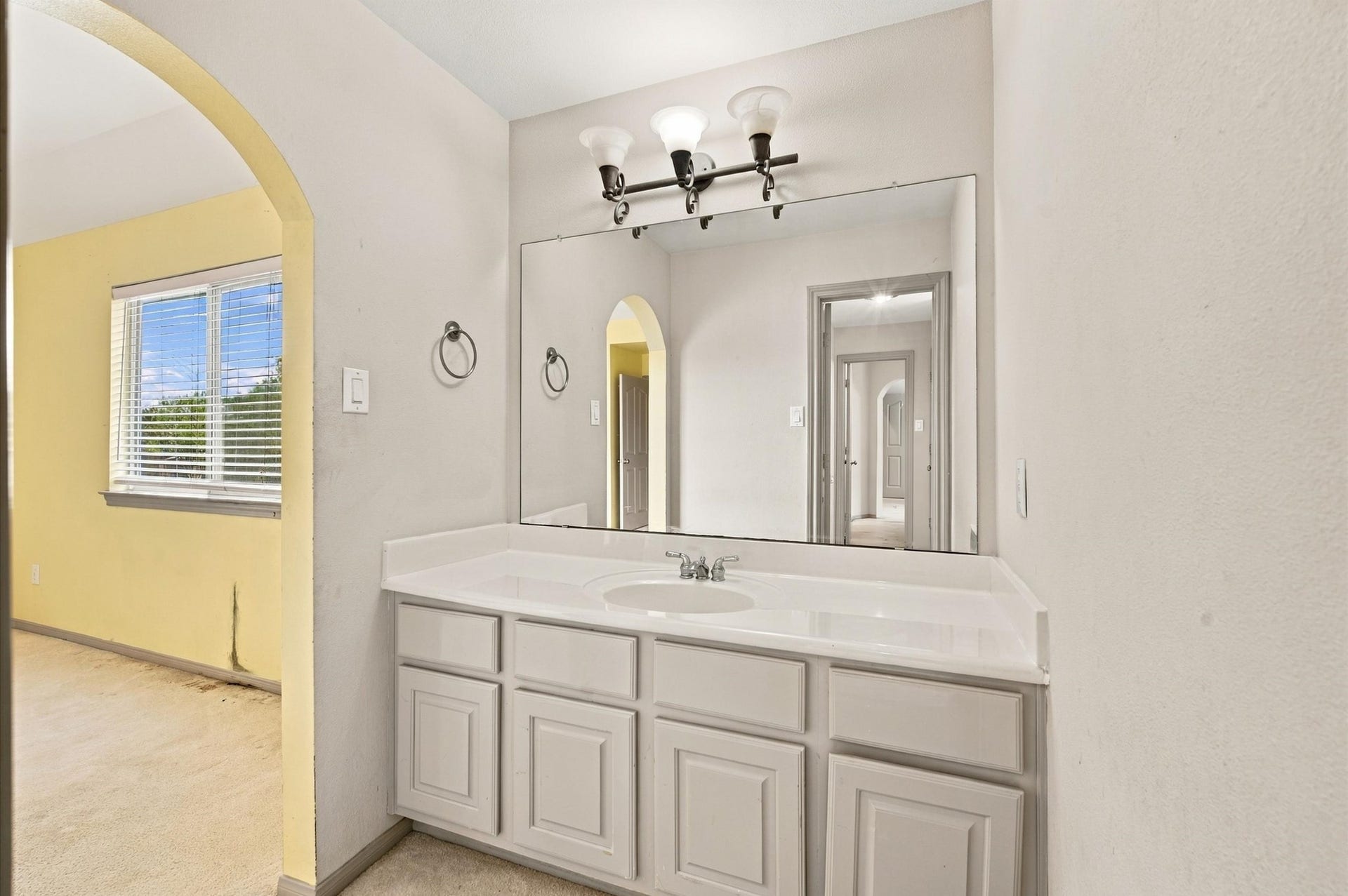 4427 Shady River, Missouri City, TX 77459 Spacious bathroom with a large mirror, ample counter space, and classic light fixtures, seamlessly connected to a bright room through an arched opening.