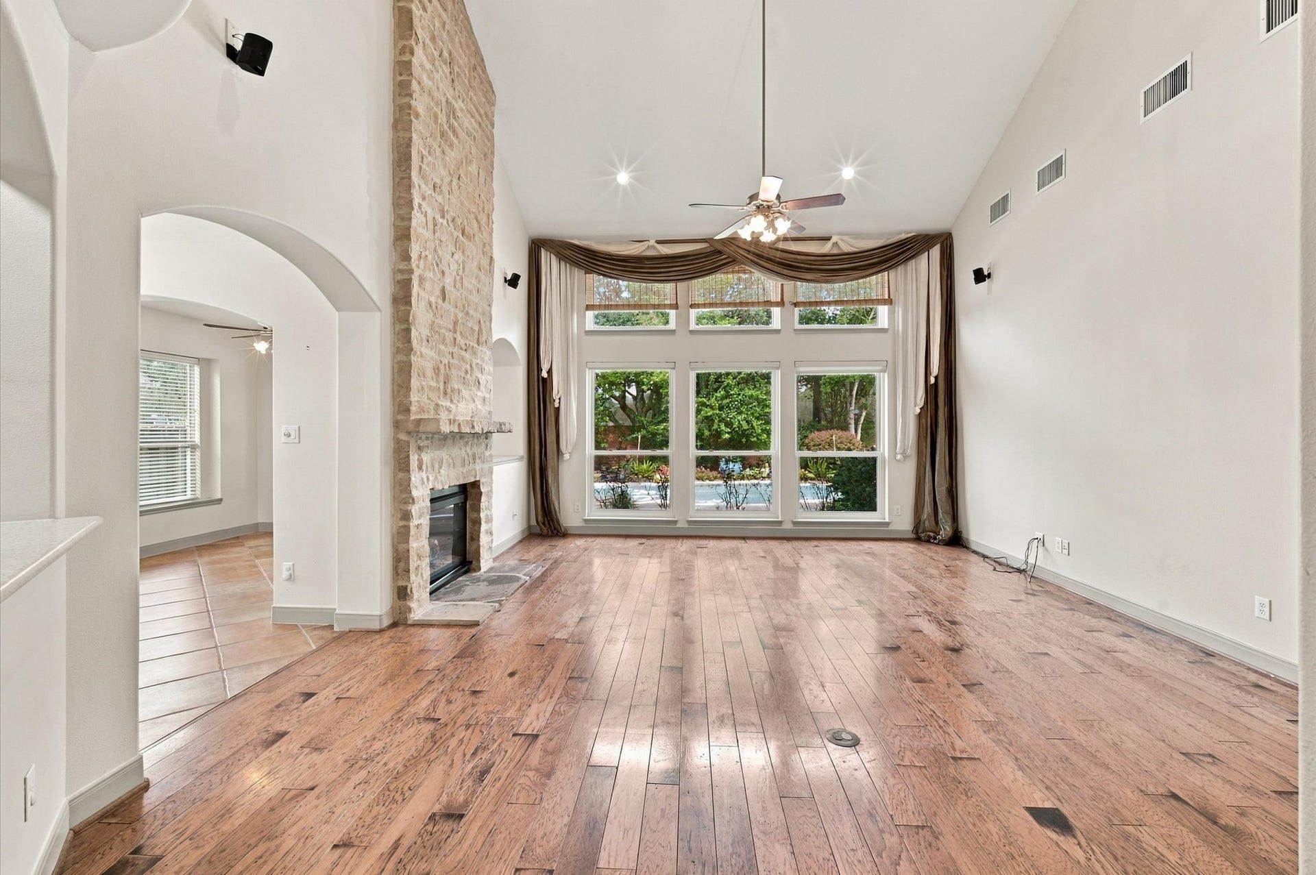 4427 Shady River, Missouri City, TX 77459 Stunning living area with soaring ceilings, a cozy stone fireplace, and expansive windows offering a view of the lush backyard. Elegant hardwood floors and an open archway enhance the spacious feel.