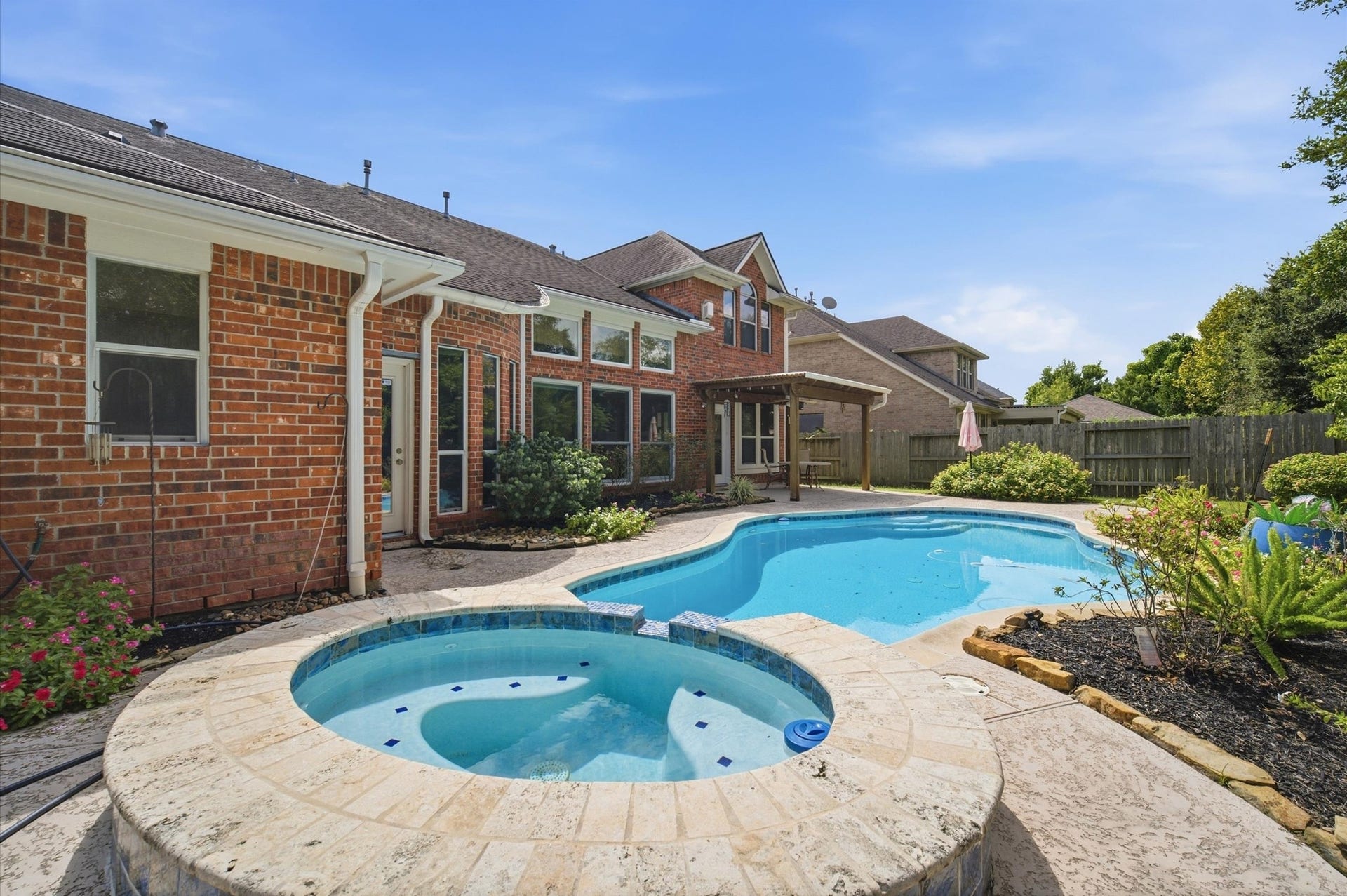 4427 Shady River, Missouri City, TX 77459 A charming backyard oasis features a sparkling pool and spa, surrounded by lush greenery and a spacious patio, perfect for relaxation and entertaining.