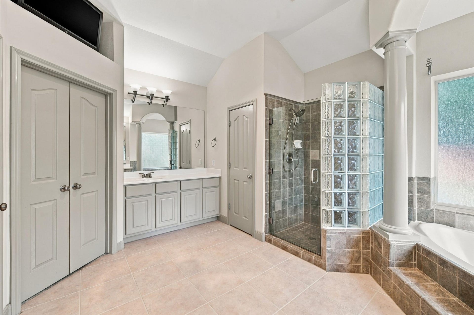 4427 Shady River, Missouri City, TX 77459 Spacious bathroom featuring a glass-enclosed shower with tile accents, a luxurious soaking tub, dual sinks with ample counter space, and elegant architectural columns.