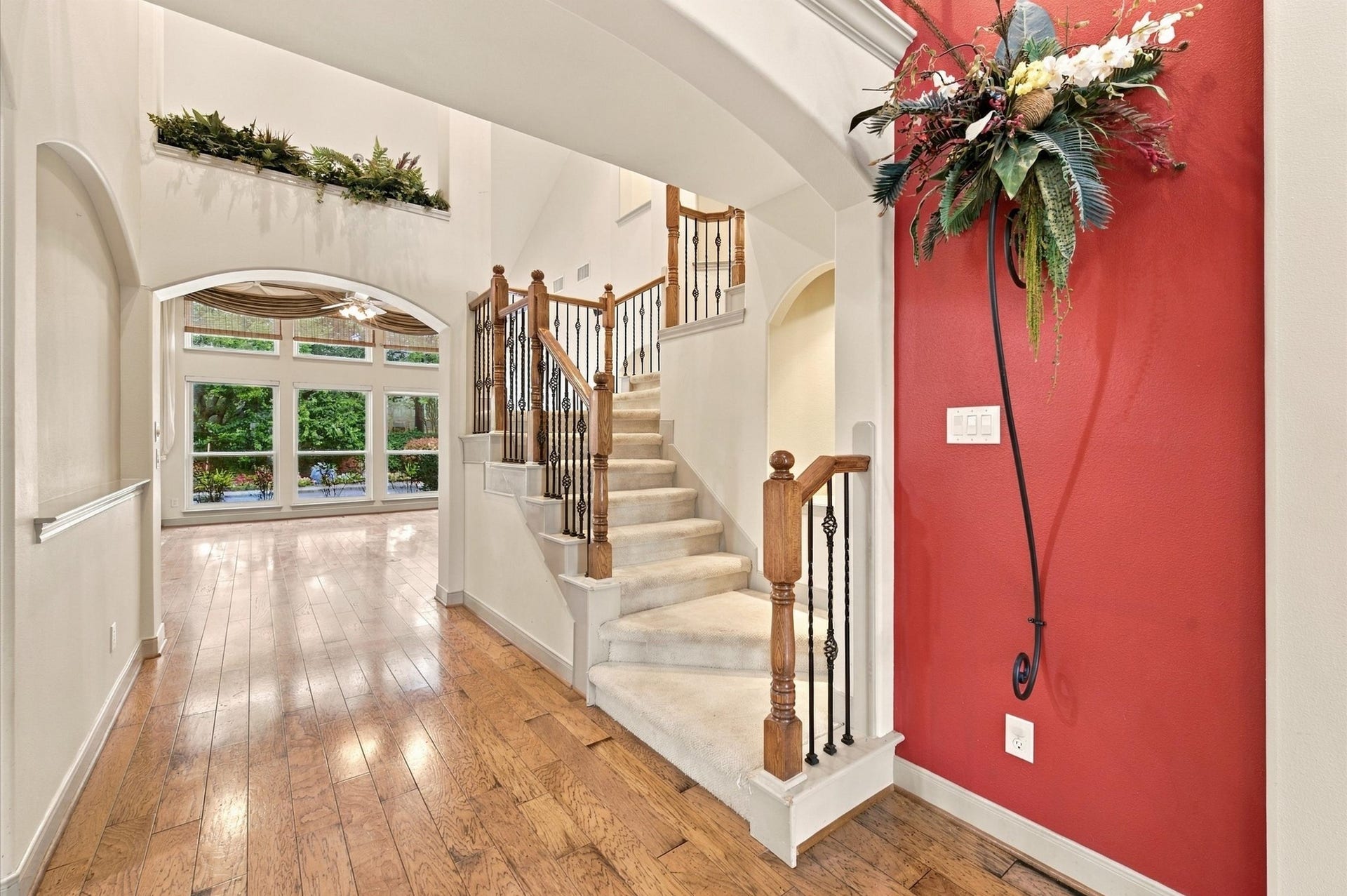 4427 Shady River, Missouri City, TX 77459 Elegant entryway featuring rich hardwood floors, a striking staircase with ornate railings, and a bold accent wall with floral decor, leading to a bright living area with expansive windows.
