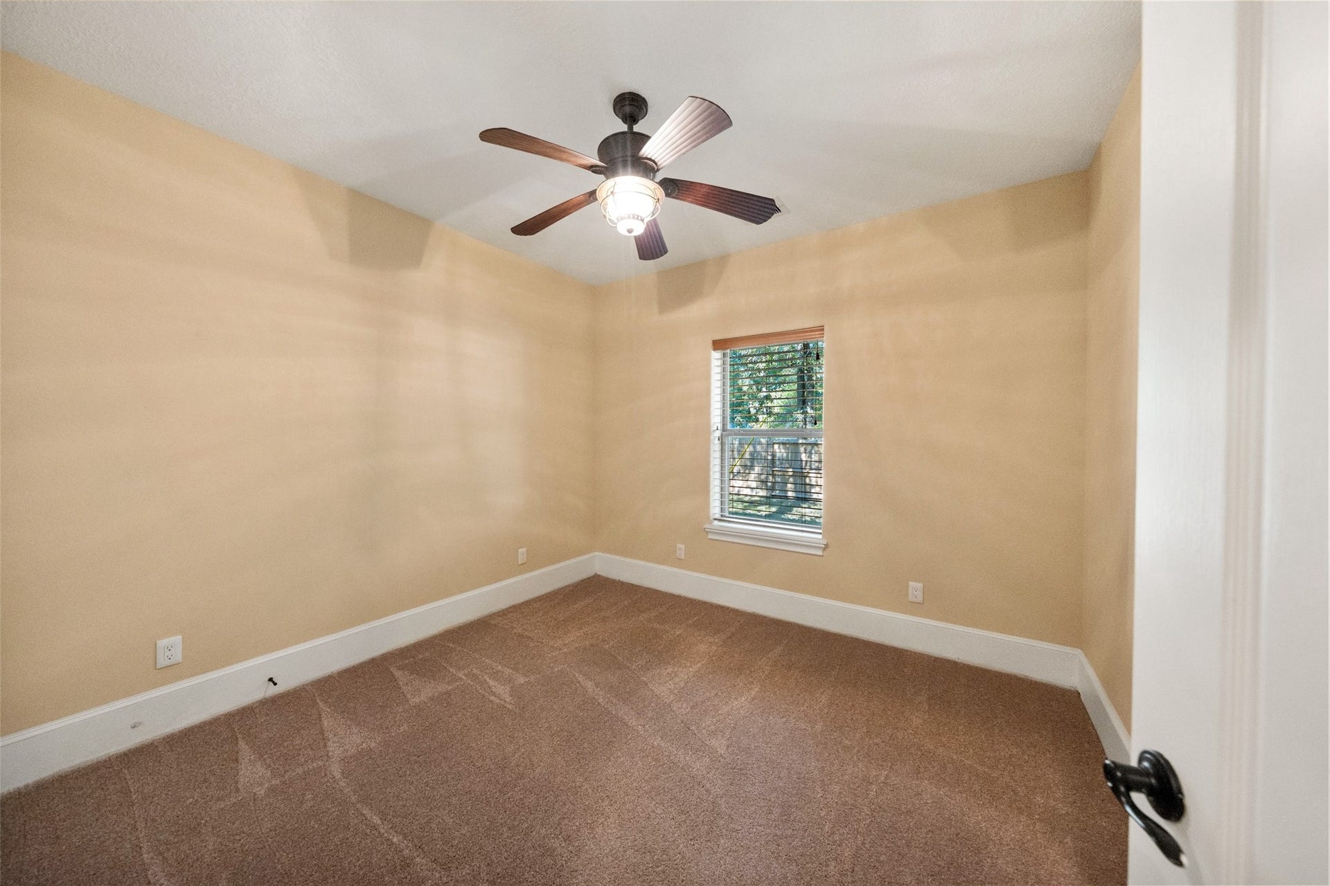 Cozy guest bedroom with soft natural light and a ceiling fan, perfect for relaxation.