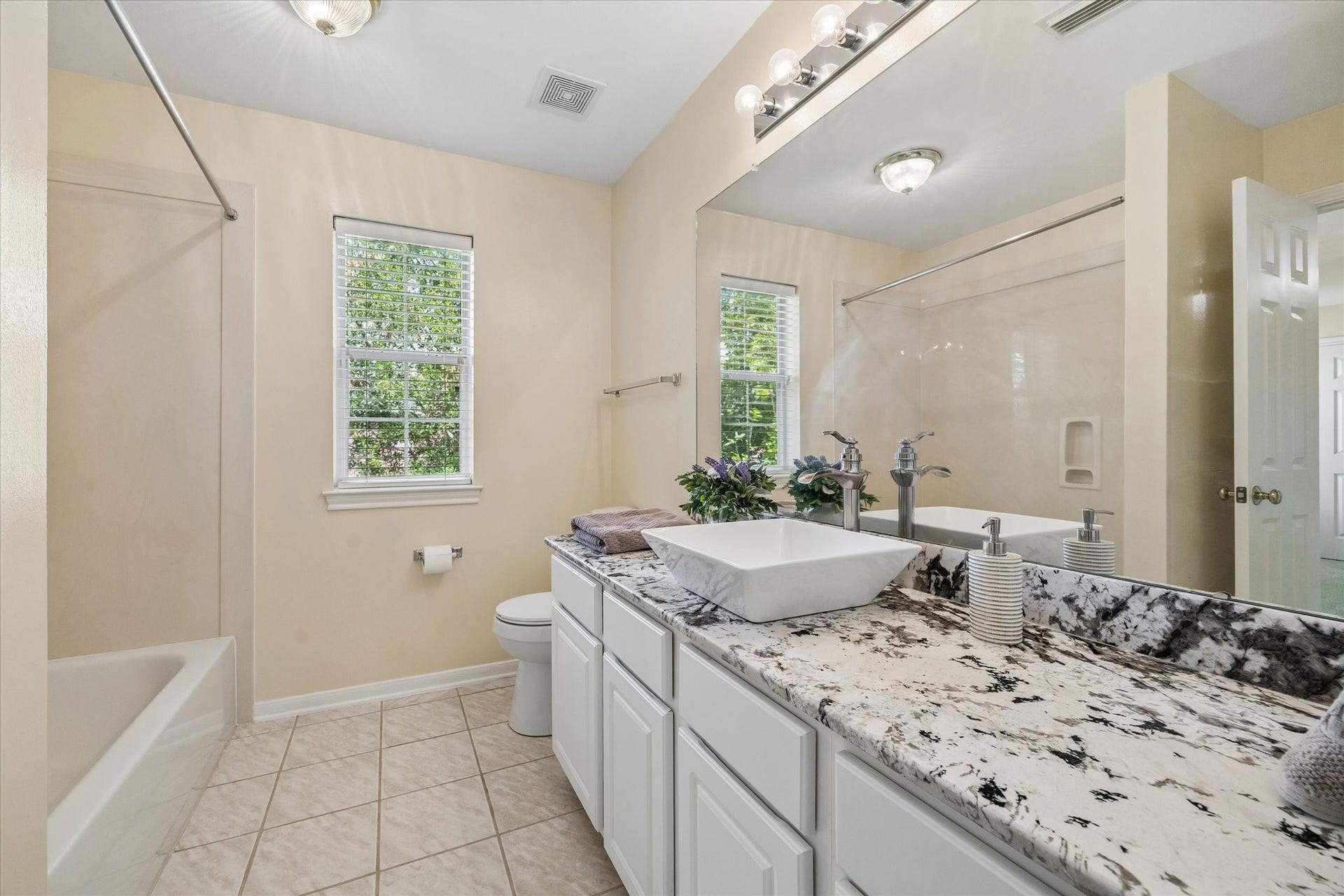 1115 Mulberry Lane, Bellaire, TX 77401 Bright bathroom featuring a stylish granite countertop with a modern vessel sink, tiled flooring, and a combination tub and shower.