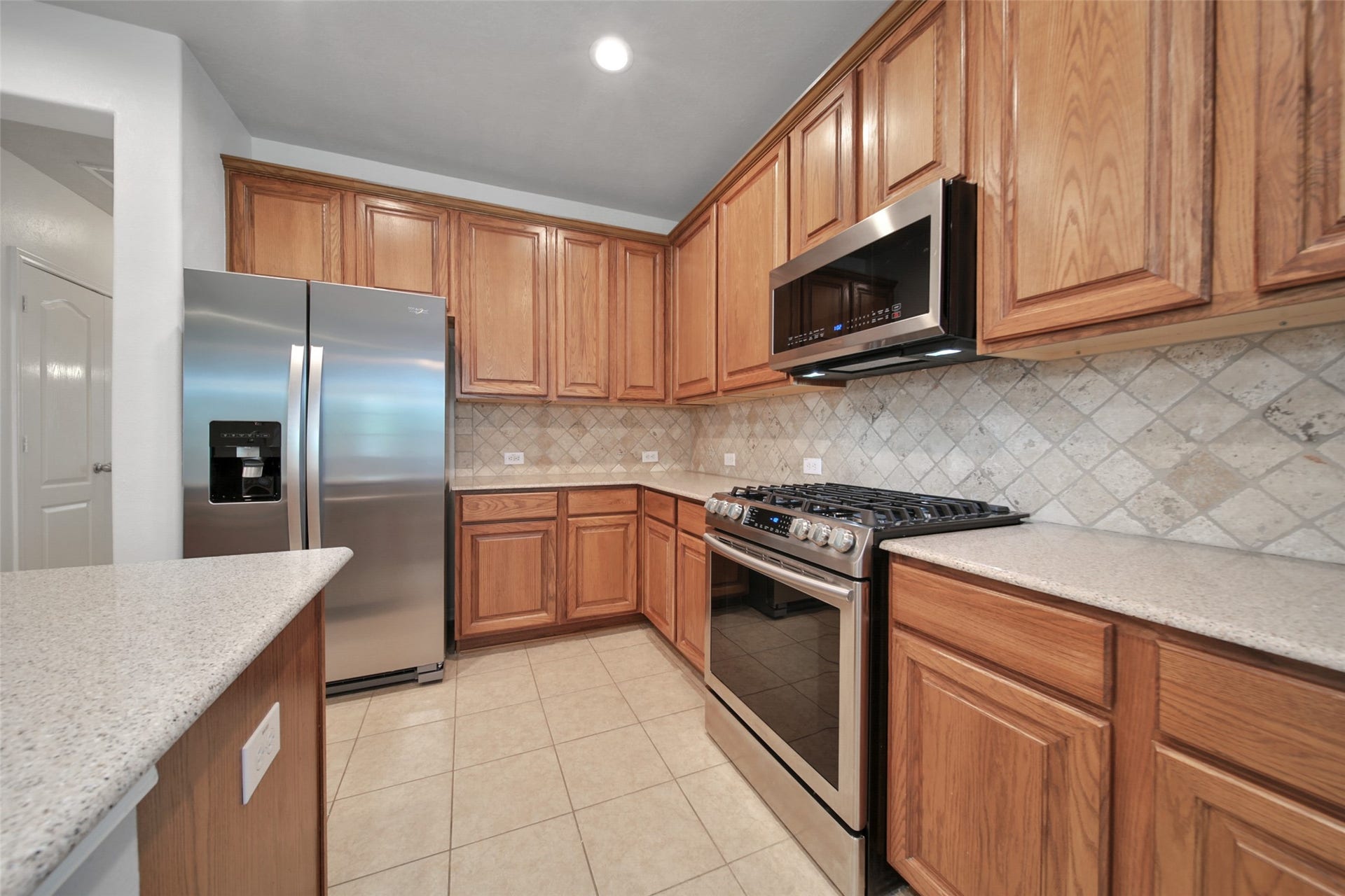 The kitchen is functional and pretty featuring quartz countertop, travertine backsplash, lots of cabinetry, Island with breakfast bar, stainless steel appliances, recessed lighting and adjacent pantry and utility room.