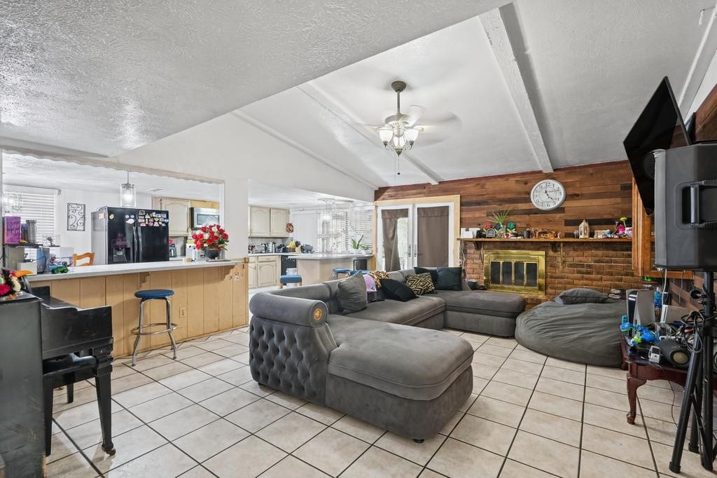 Spacious living area with vaulted ceilings, cozy sectional seating, and a charming brick fireplace, seamlessly connecting to a bright kitchen and breakfast bar.