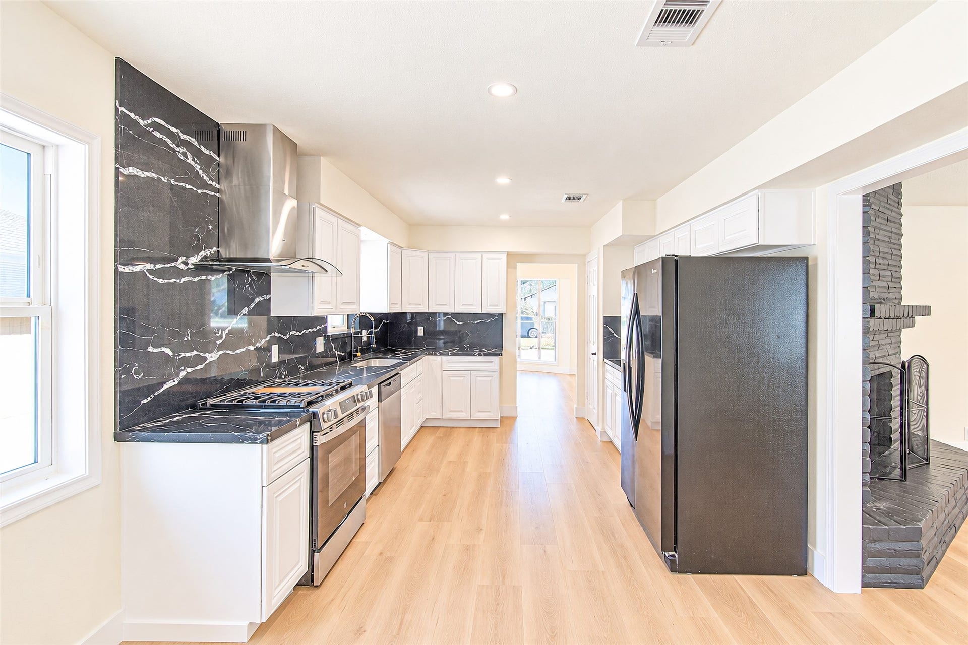 7623 Braes Meadow Drive, Houston, TX 77071 A sleek modern kitchen with elegant black quartz countertops, stainless steel appliances, and crisp white cabinetry, enhanced by warm wooden flooring and abundant natural light.