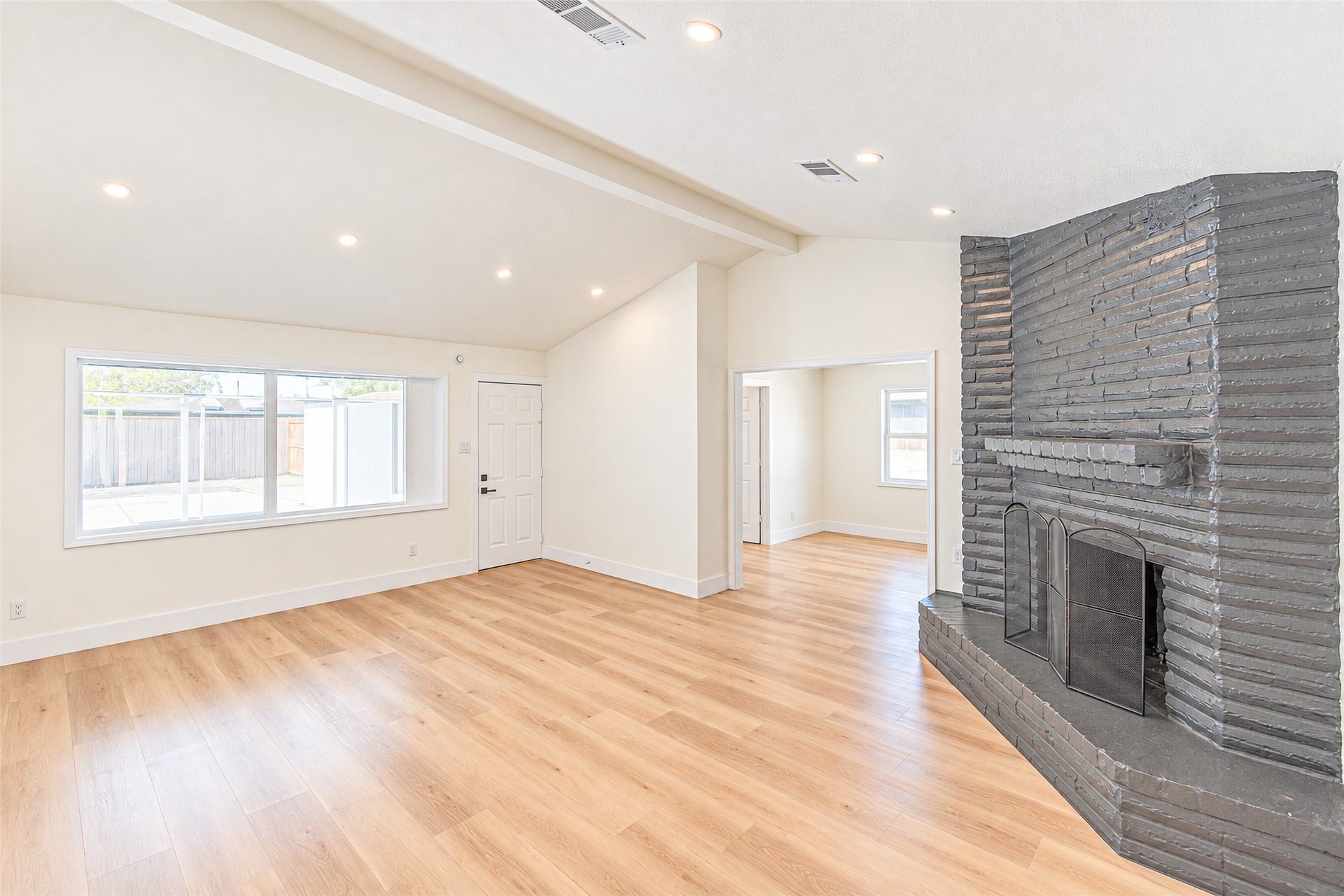 7623 Braes Meadow Drive, Houston, TX 77071 Bright and airy living room with vaulted ceilings, featuring a striking brick fireplace and luxury vinyl flooring, complemented by large windows that flood the space with natural light.