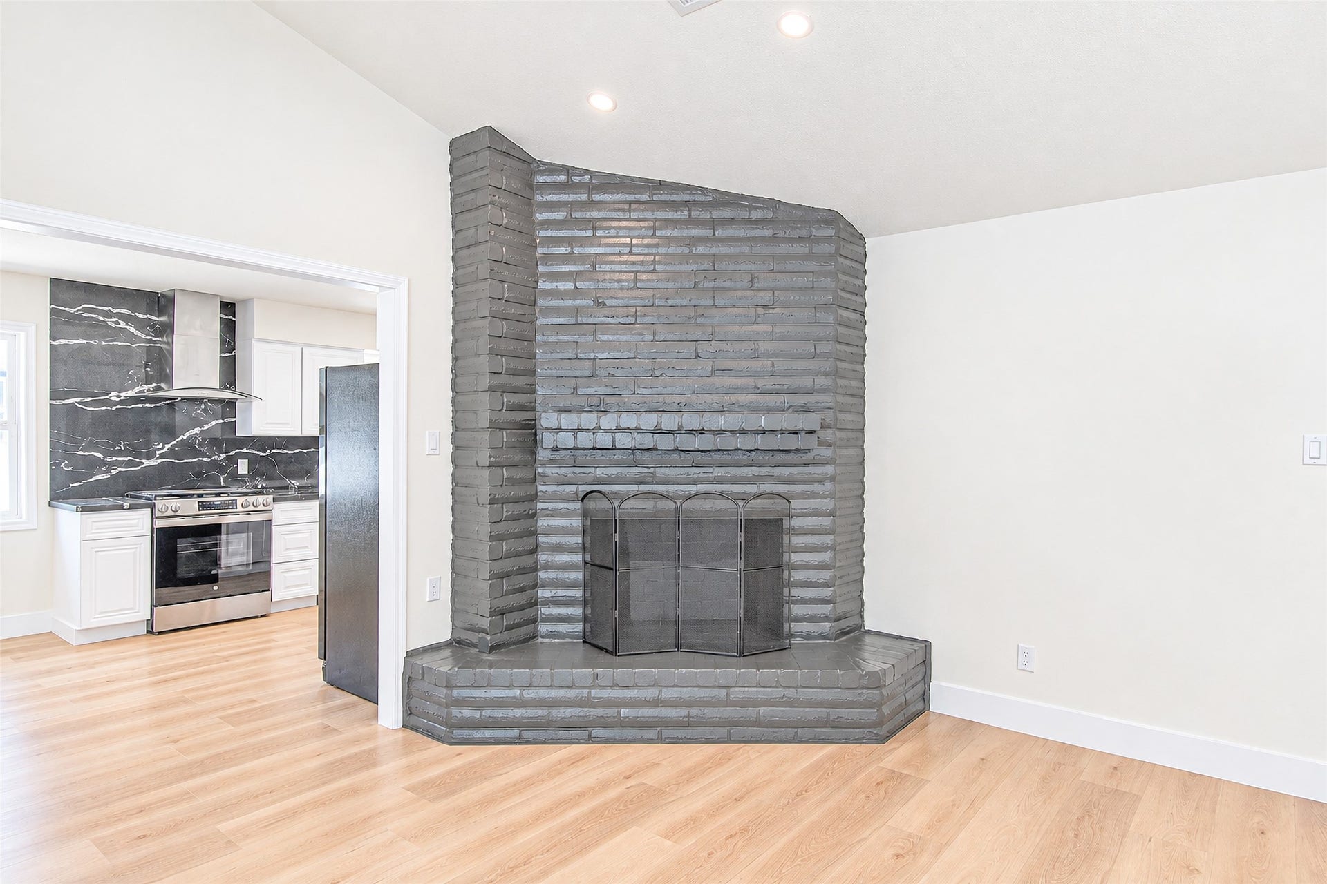 7623 Braes Meadow Drive, Houston, TX 77071 Charming living area with a striking gray brick fireplace, seamlessly flowing into a modern kitchen featuring sleek marble accents and stainless steel appliances.