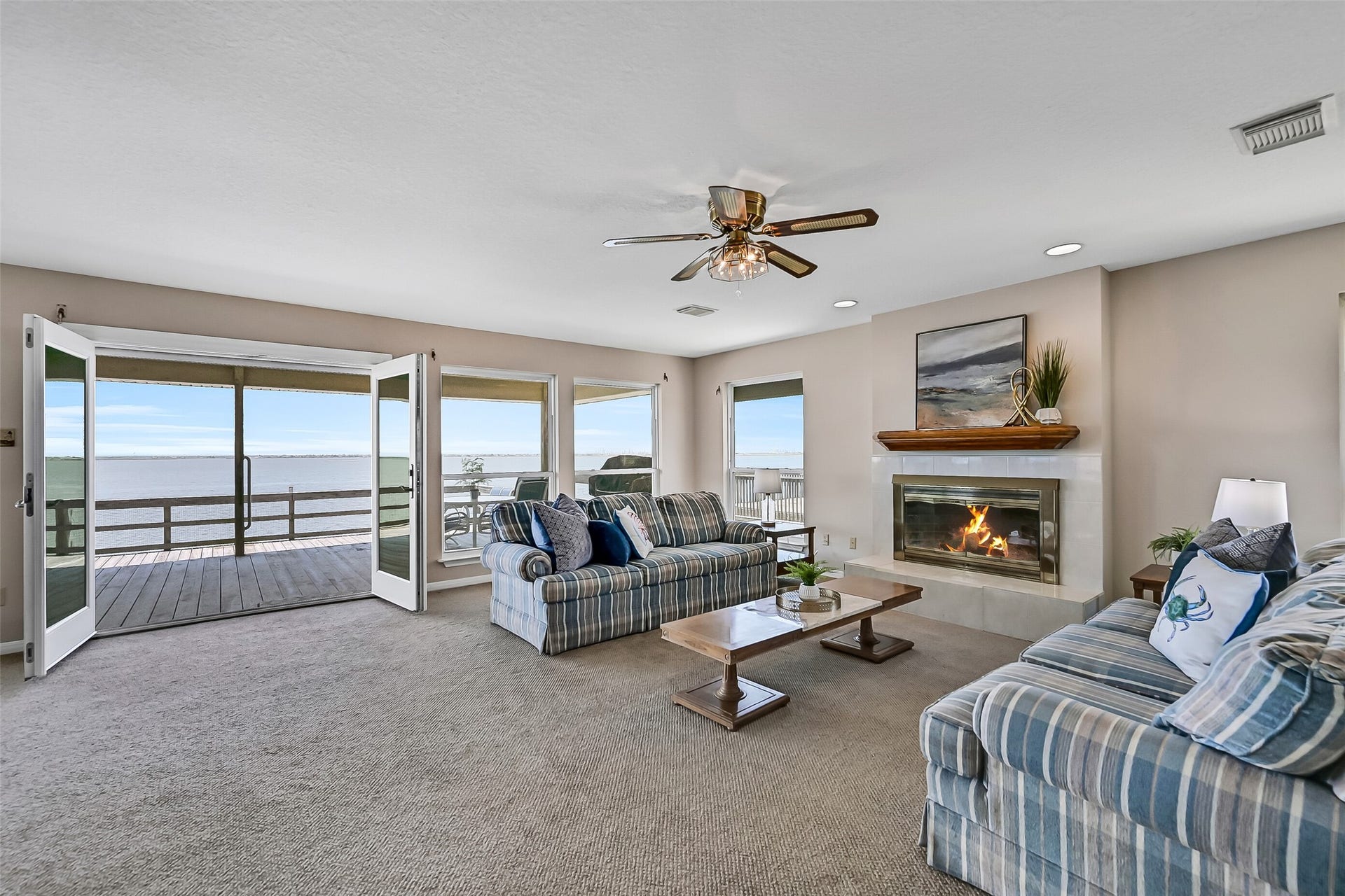 243 Isles End Road, #RR2, Tiki Island, TX 77554 The living room is truly the heart of the home, featuring a wood-burning fireplace with gas starter, fresh neutral paint, and walls of windows that frame breathtaking panoramic views of West Bay. French doors open directly onto the expansive waterfront deck.