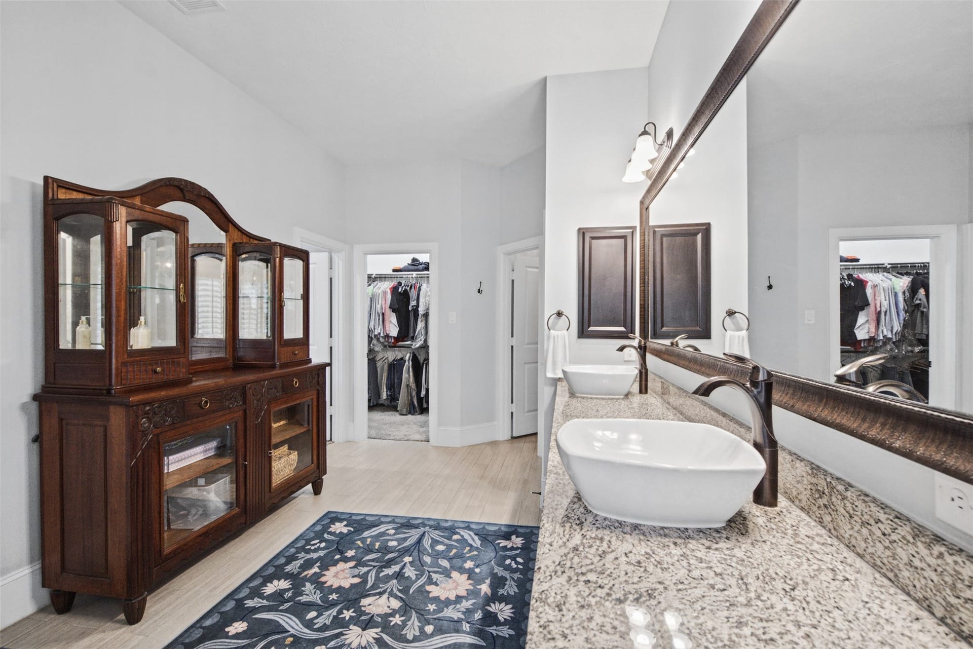 Luxurious primary bathroom featuring elegant tile floors, granite countertops, and a view toward the spacious closet area.
