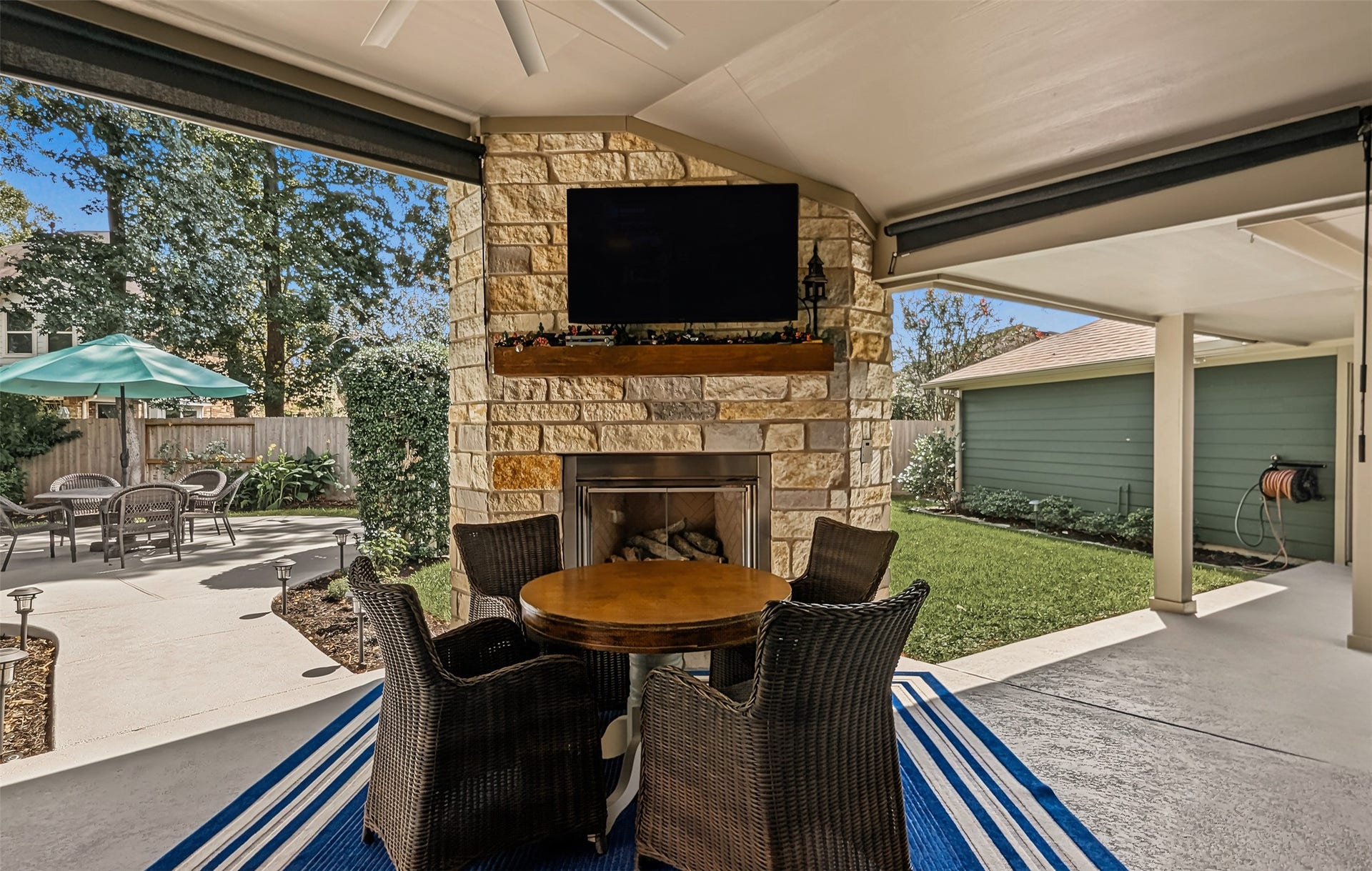 Dine al fresco by the cozy stone fireplace in this serene outdoor retreat. The covered area features pull-down shades, a TV, and a cool deck coating for ultimate relaxation.