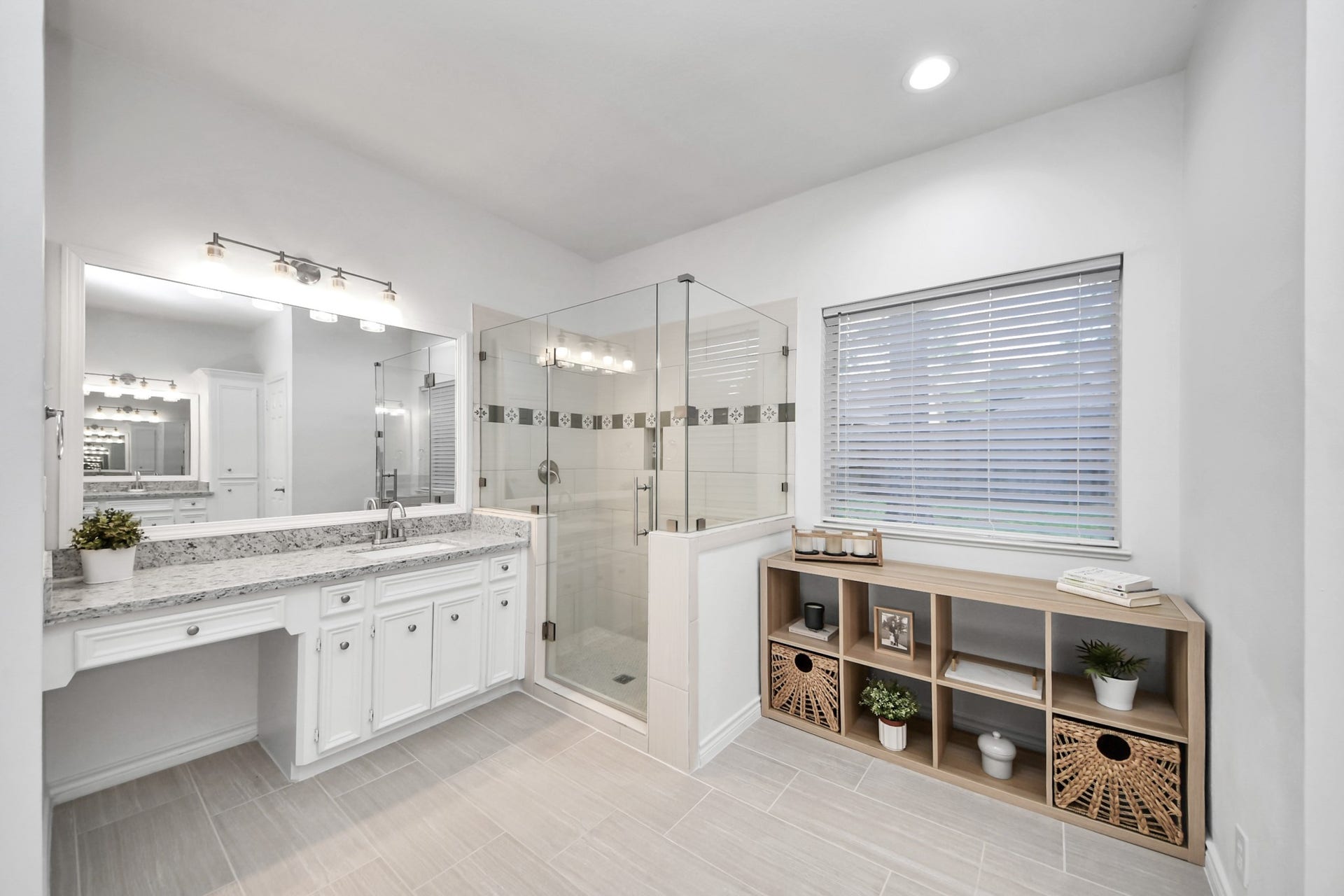 New glass-enclosed shower, elegant vanities with granite countertop, and ample natural light from a large window.