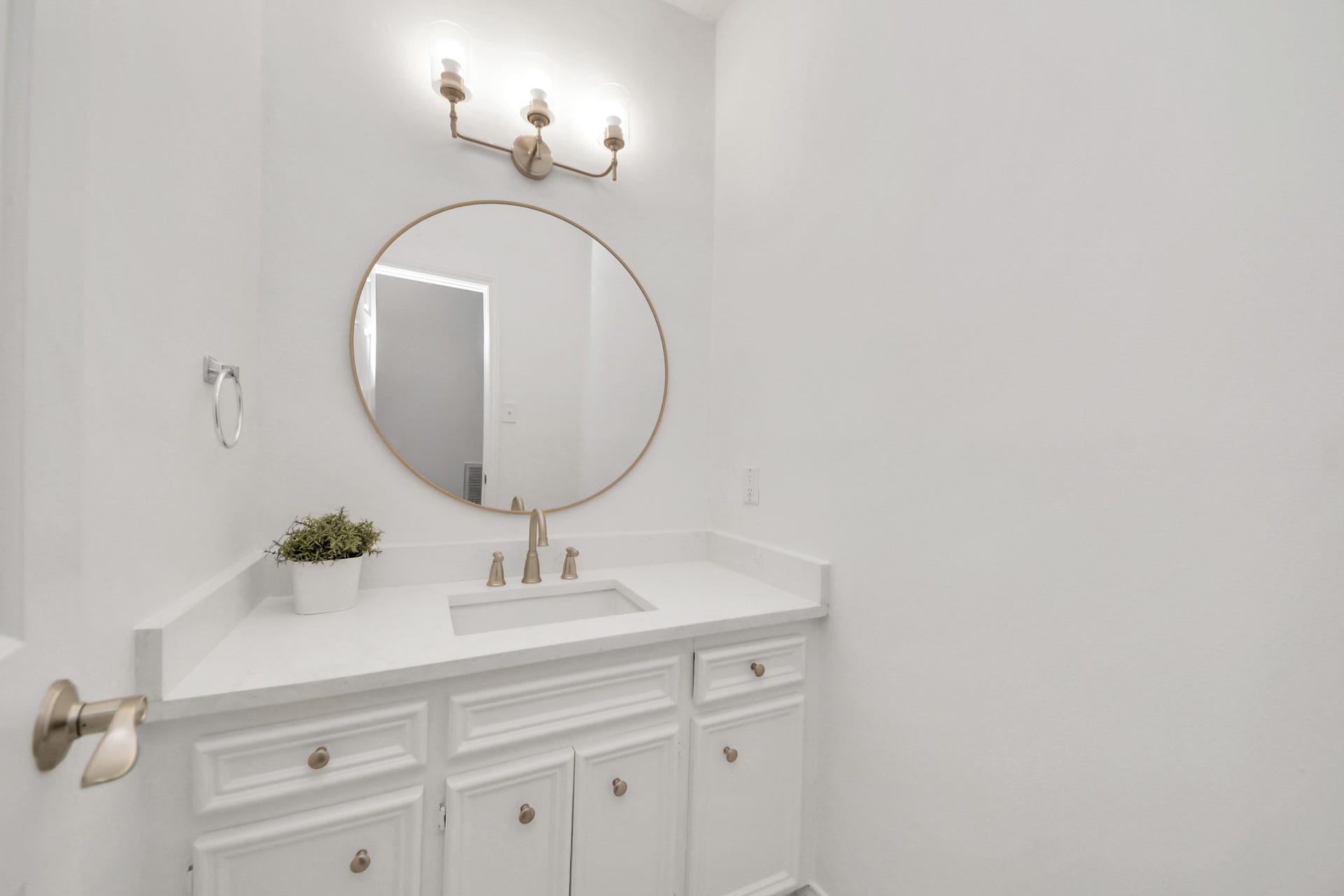 Full bathroom with a sleek white vanity, a round mirror, and stylish brass fixtures, creating a modern space.