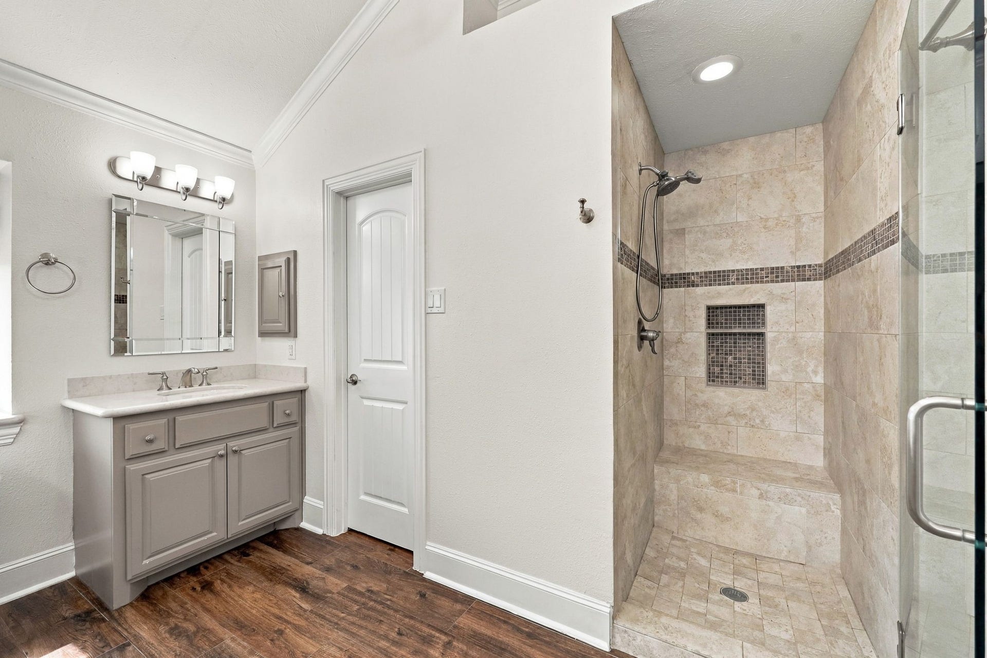 33211 Woodton Court, Weston Lakes, TX 77441 The large walk-in shower features a frameless glass door, a built-in bench, floor-to-ceiling tiled walls with an elegant accent strip, a brushed nickel showerhead and handheld wand, and convenient built-in niches for shampoo, soap, and other bath essentials.