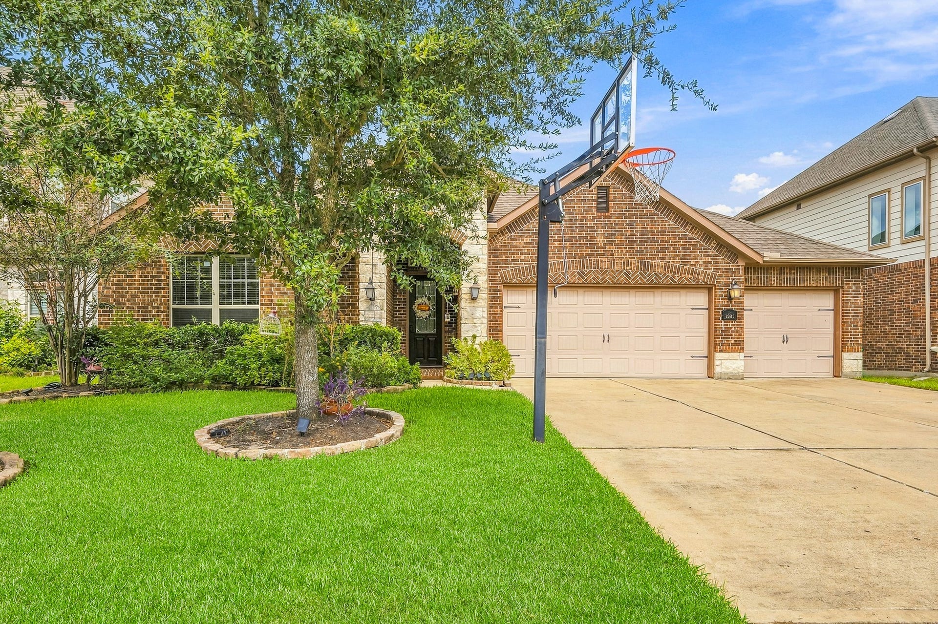 25610 Buckley Bluff Lane, Katy, TX 77494 Charming brick home featuring a spacious three-car garage, lush landscaping, and a basketball hoop for outdoor fun.