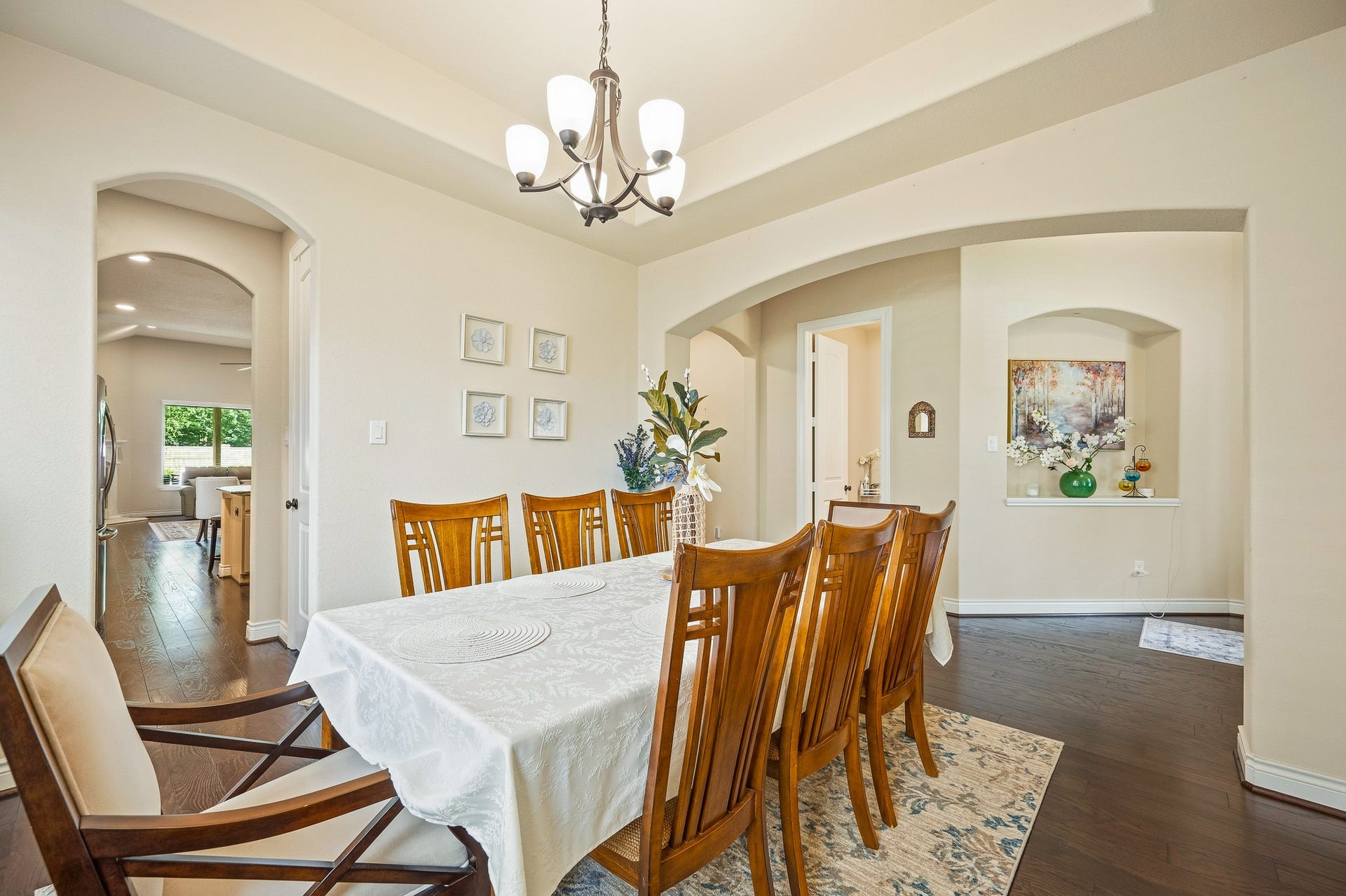25610 Buckley Bluff Lane, Katy, TX 77494 Experience the elegance of a dining room featuring a long wooden table with a white tablecloth and matching chairs beneath a stylish chandelier, seamlessly connected to open kitchen and living spaces through graceful archways, enhancing the home's flow and charm.