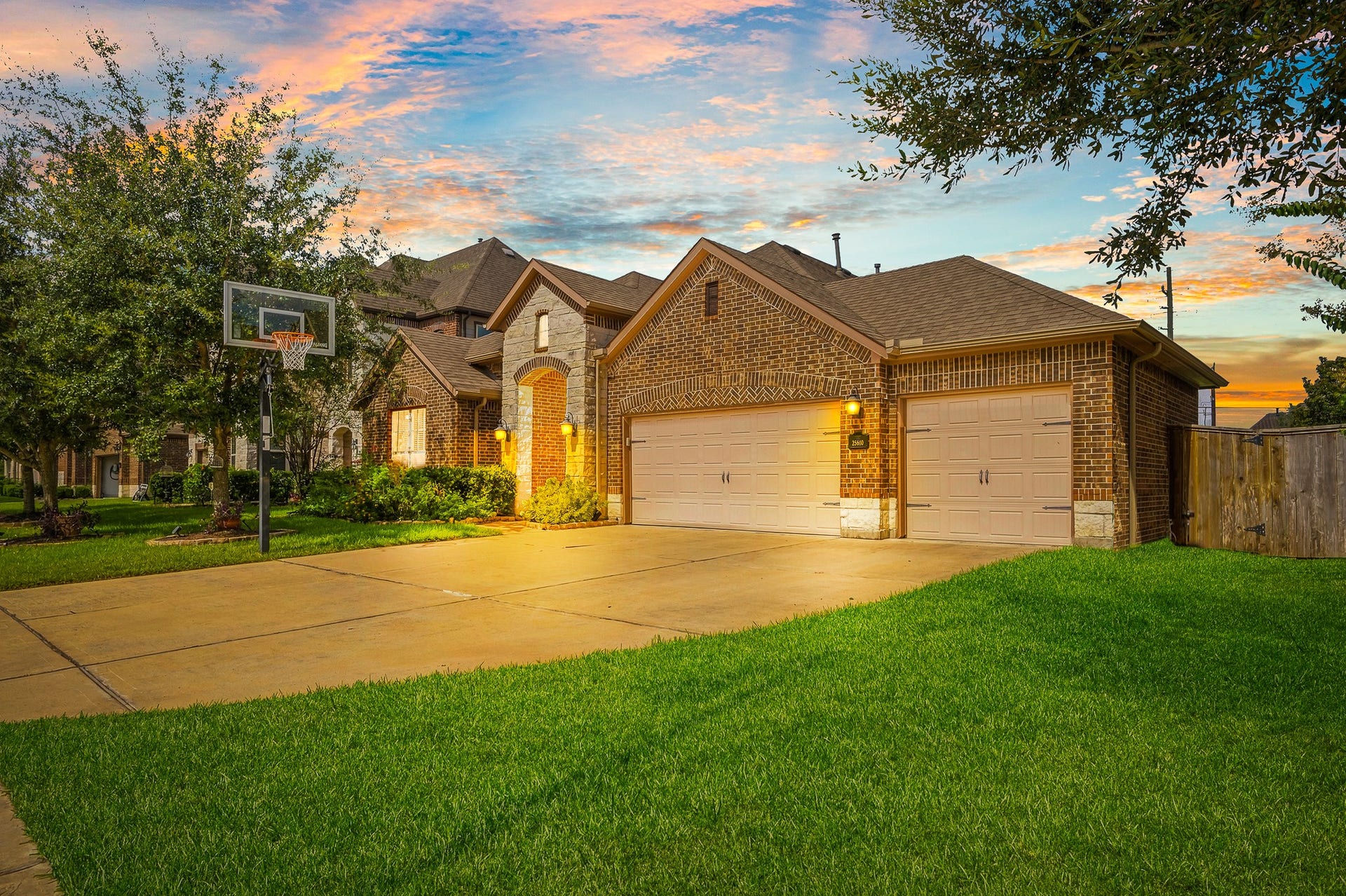 25610 Buckley Bluff Lane, Katy, TX 77494 Experience the charm of this stunning brick home with a spacious three-car garage, beautifully landscaped front yard, and a basketball hoop, all set against a breathtaking sunset backdrop.