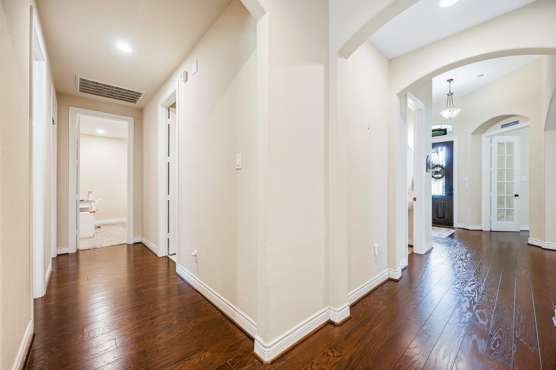 25610 Buckley Bluff Lane, Katy, TX 77494 An elegant hallway with rich wood flooring, soft lighting, and arched doorways warmly invites you into spacious rooms, creating an inviting atmosphere.