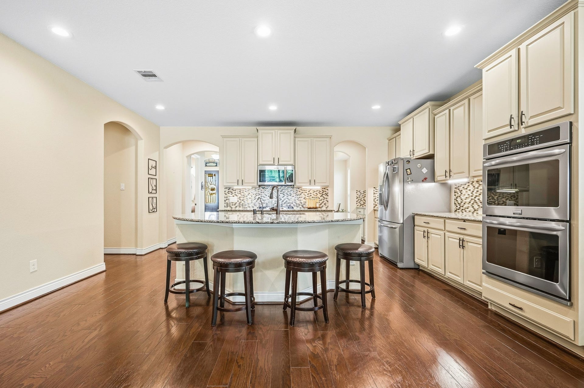 25610 Buckley Bluff Lane, Katy, TX 77494 Experience culinary elegance in this spacious kitchen featuring exquisite cabinetry, a large center island with seating, modern stainless steel appliances, a stylish backsplash, and rich hardwood floors.