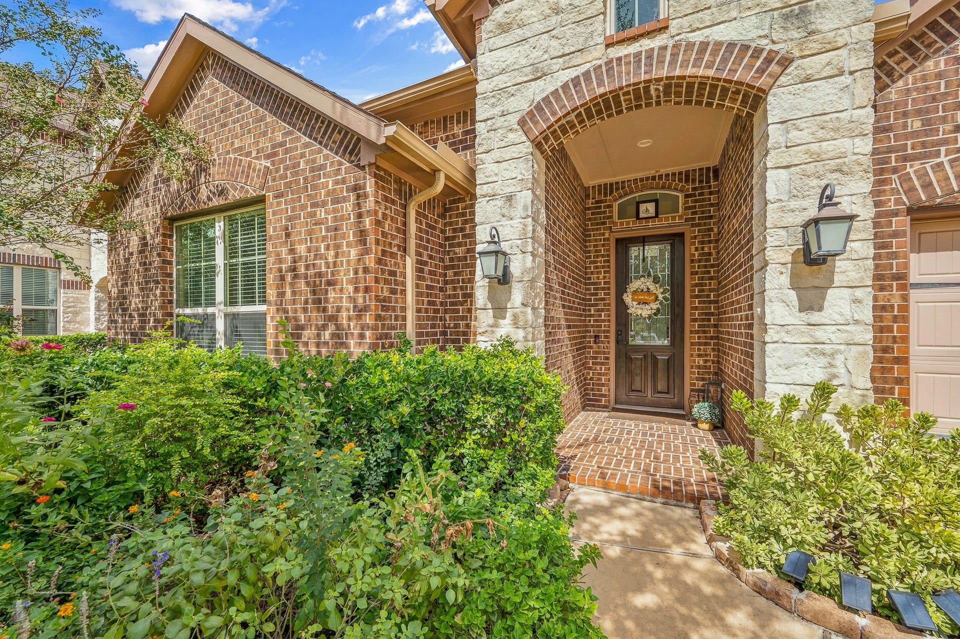 25610 Buckley Bluff Lane, Katy, TX 77494 Charming brick exterior with a welcoming arched entryway, surrounded by lush landscaping and enhanced by decorative lanterns for a warm, inviting atmosphere.
