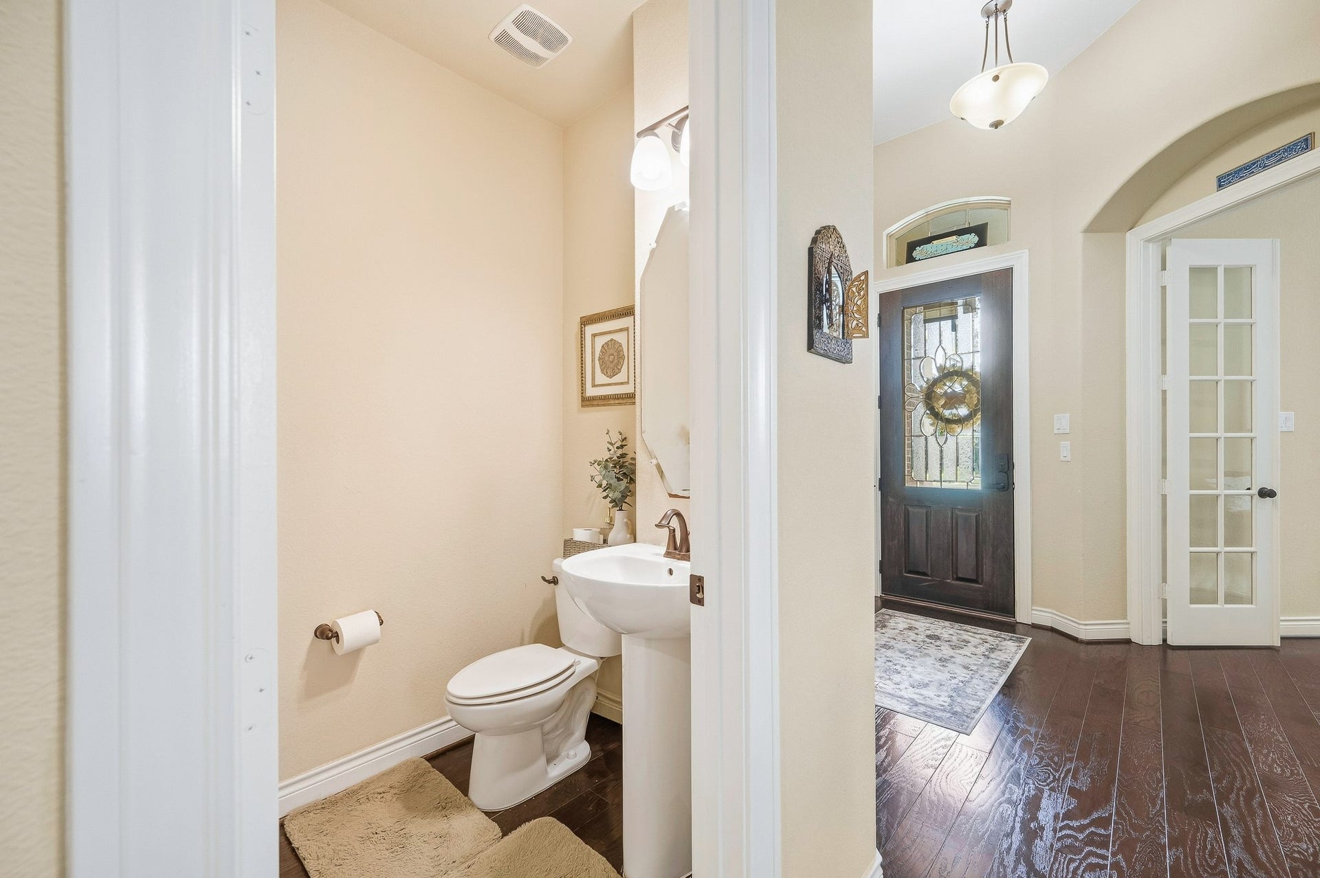 25610 Buckley Bluff Lane, Katy, TX 77494 Charming entryway with elegant dark wood flooring and a welcoming glass-paneled door leads seamlessly to a cozy powder room featuring modern fixtures and warm lighting.