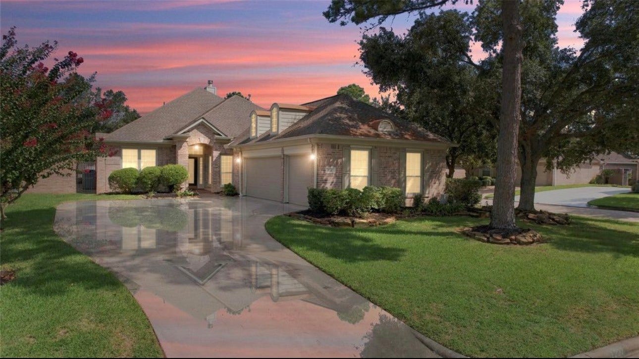 Charming single-story home with a beautifully manicured lawn, inviting driveway, and elegant brick exterior, set against a stunning sunset backdrop.