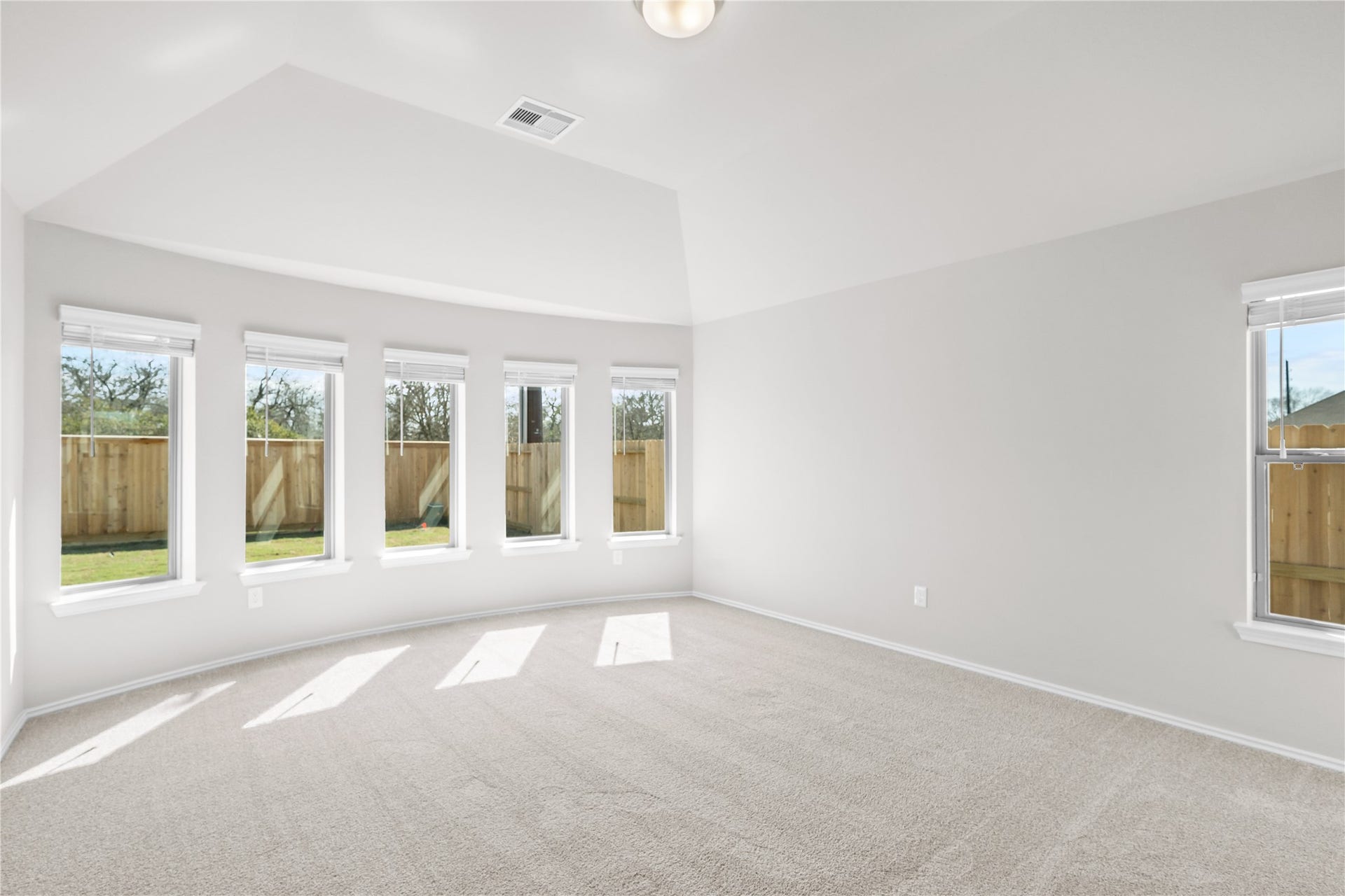 A wall of five windows fills the primary suite with natural light beneath a vaulted ceiling.