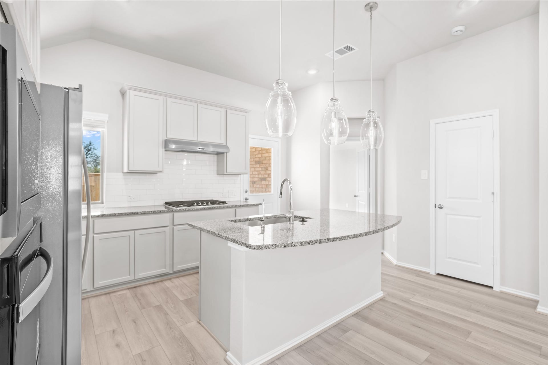 The kitchen is anchored by a granite island, with white shaker cabinetry, subway tile backsplash and pendant lighting.