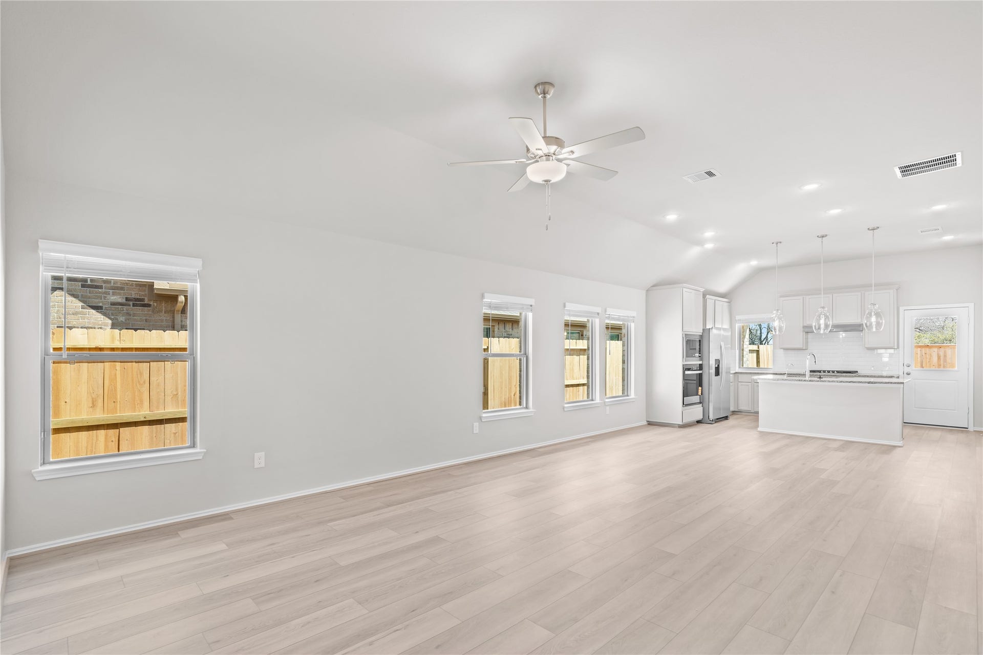 The family room flows effortlessly into the kitchen beneath a vaulted ceiling, with luxury vinyl plank flooring and recessed lighting throughout.