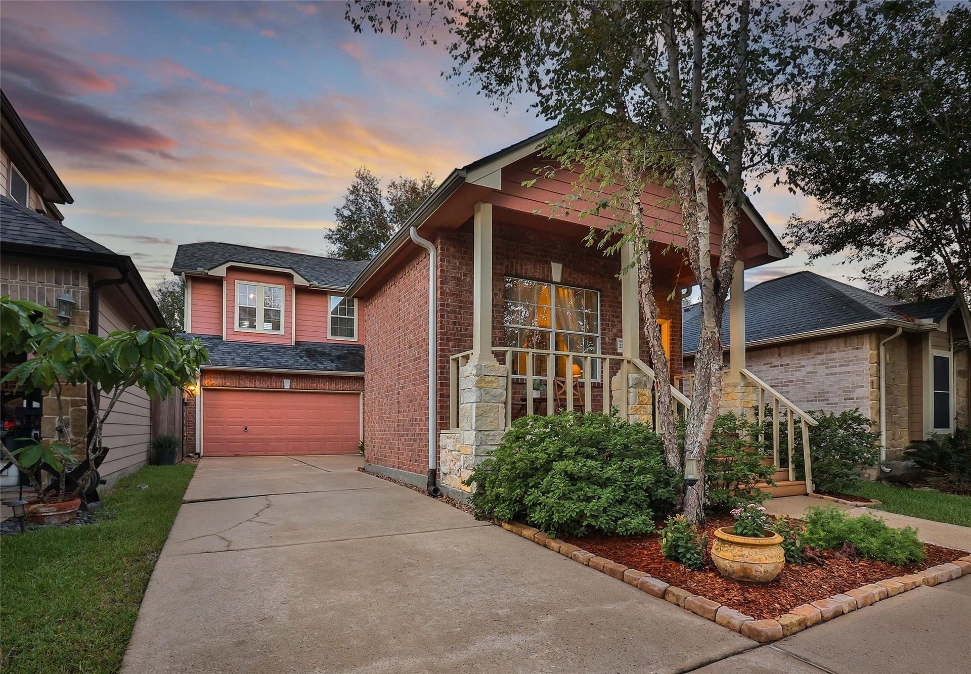 Charming two-story home featuring a brick facade, an attached garage, and mature landscaping, set against a picturesque twilight sky.