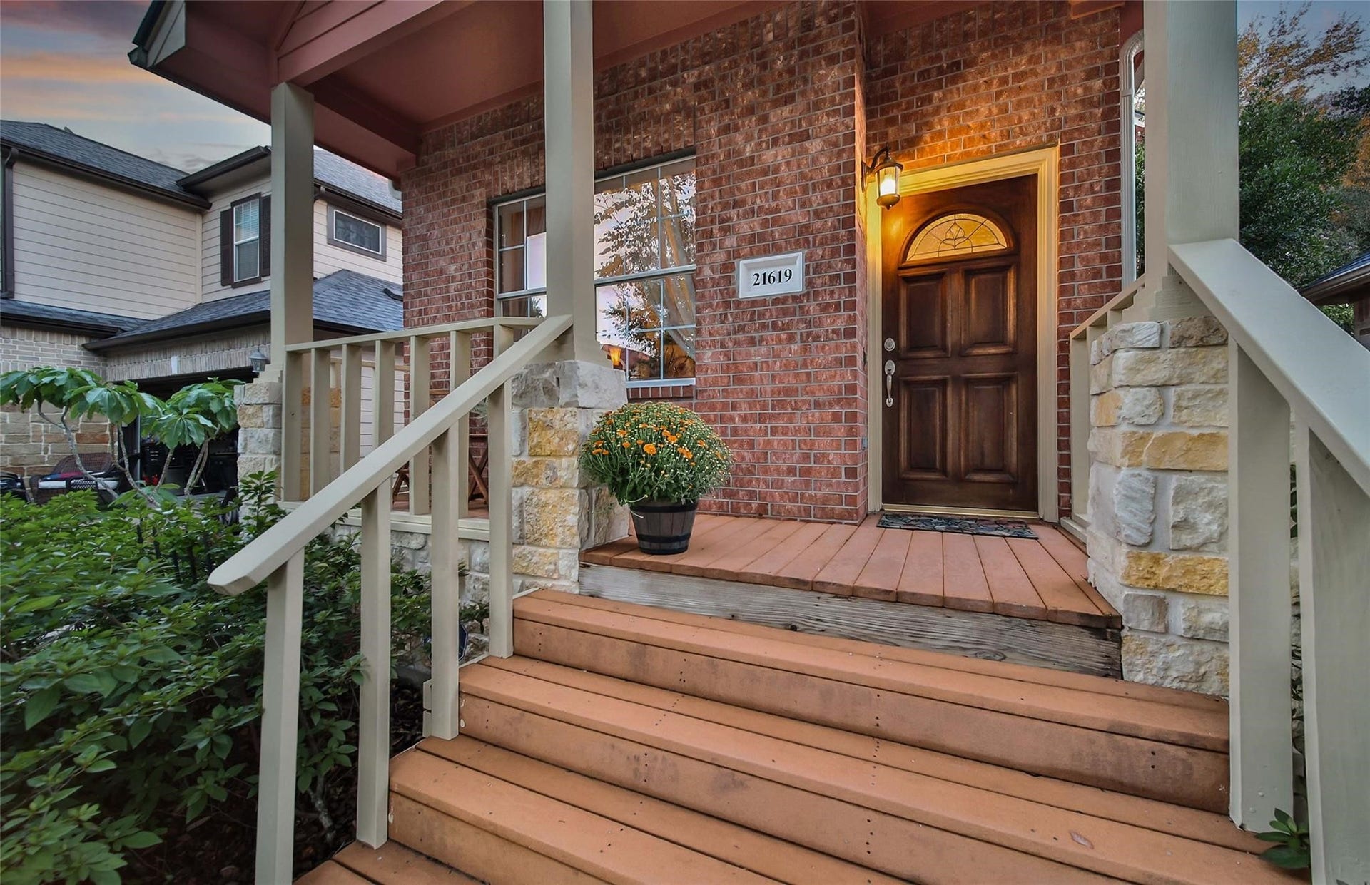Charming entrance with a warm wooden door, stone accents, and a cozy porch flanked by lush greenery, inviting a sense of home.