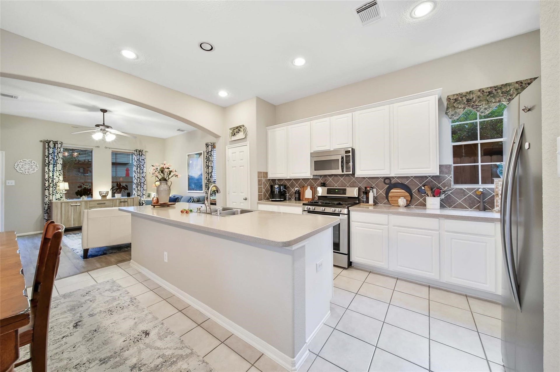 This is a bright, spacious kitchen with modern appliances, white cabinetry, and a central island that provides additional counter space and potential seating. The room features tile flooring and opens into an adjoining dining or living area, creating an open floor plan ideal for entertaining.