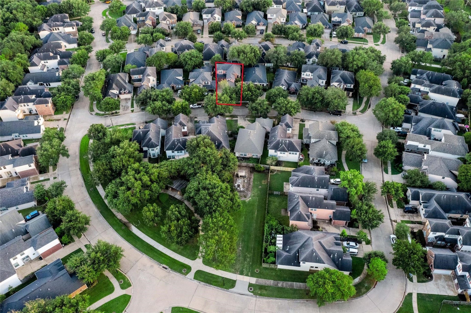 This is an aerial view of a residential neighborhood with a two-story house highlighted. The home is nestled in a well-established, tree-lined area with a spacious backyard, offering a sense of community and greenery.