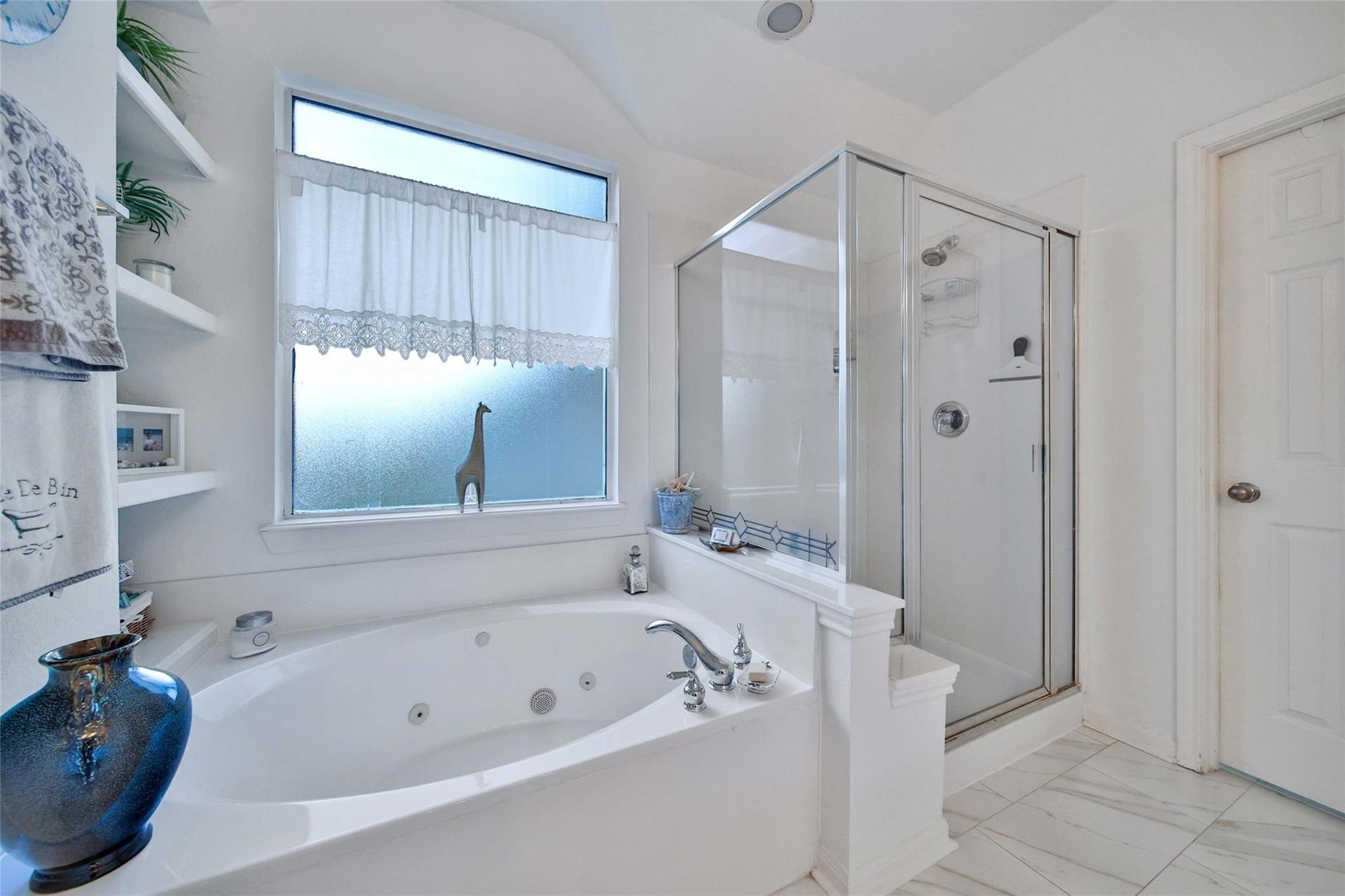 This is a bright and clean bathroom featuring a double vanity with ample storage, large mirrors, a glass-enclosed shower, and tiled flooring. It's well-lit and appears spacious.