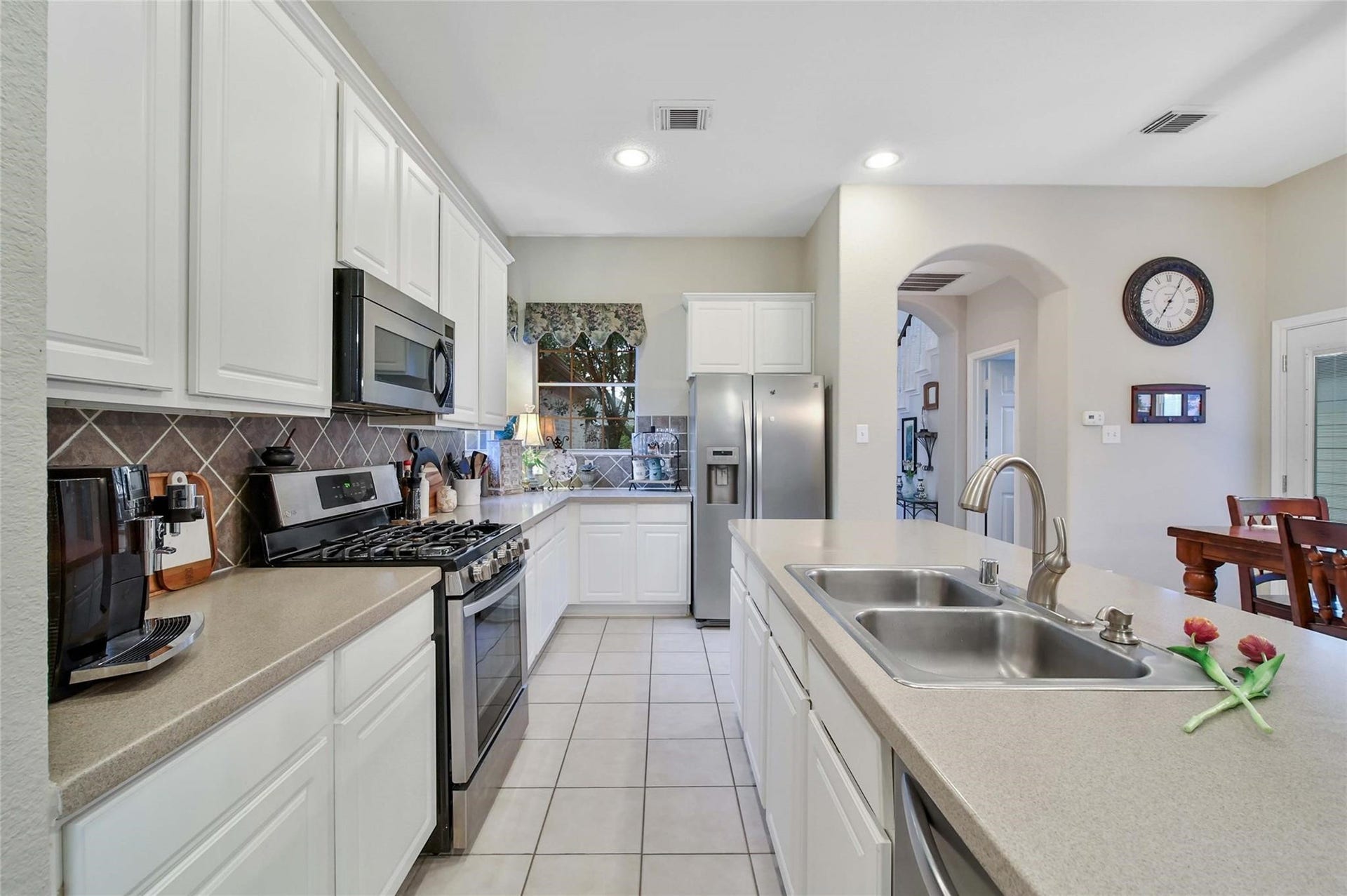 This is a bright, modern kitchen featuring white cabinetry, granite countertops, stainless steel appliances, and a double basin sink. The kitchen opens to a dining area, creating an inviting space for cooking and entertaining.