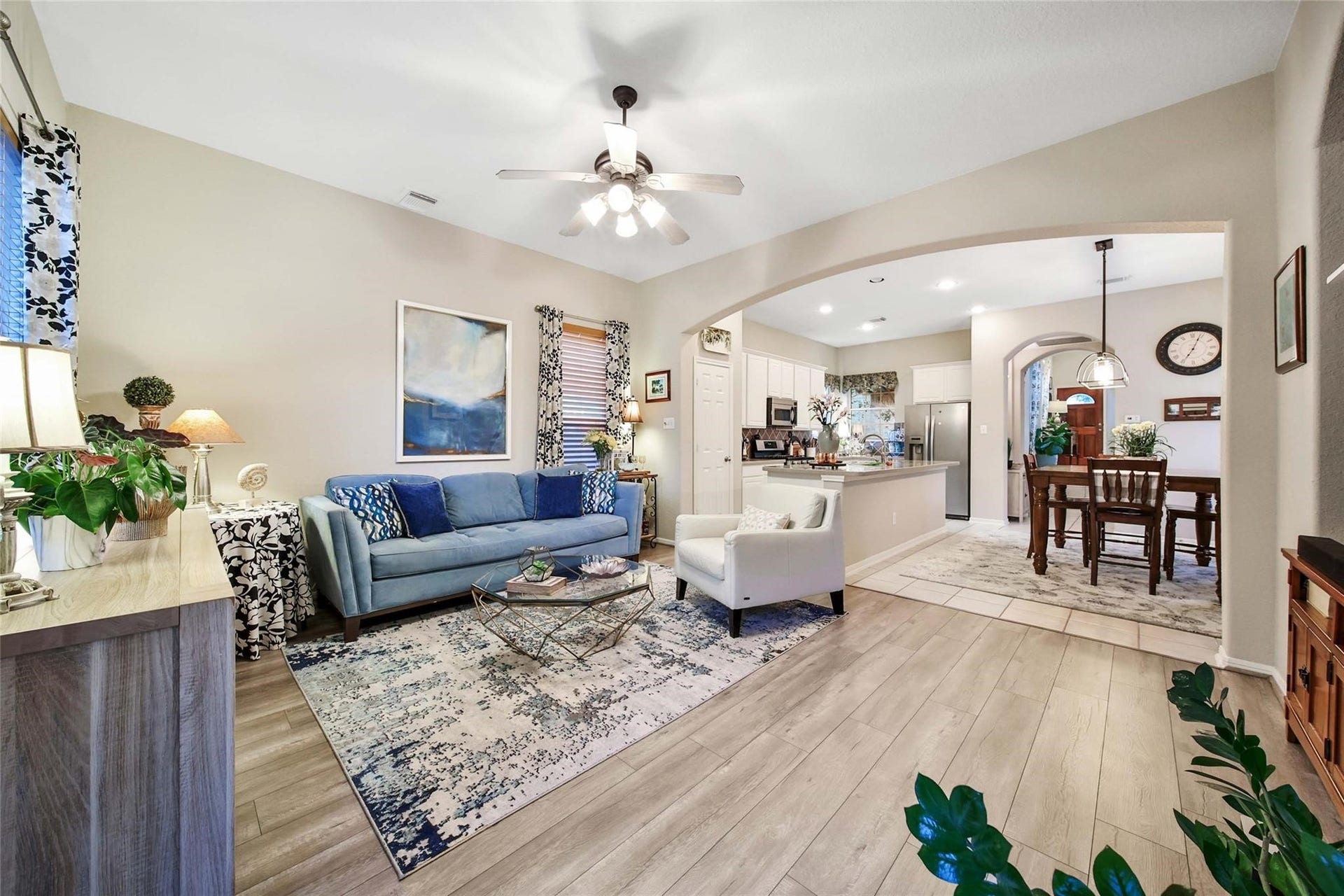 This is a spacious and modern living room featuring hardwood floors, a high ceiling with a fan, an accent blue wall, and large windows.