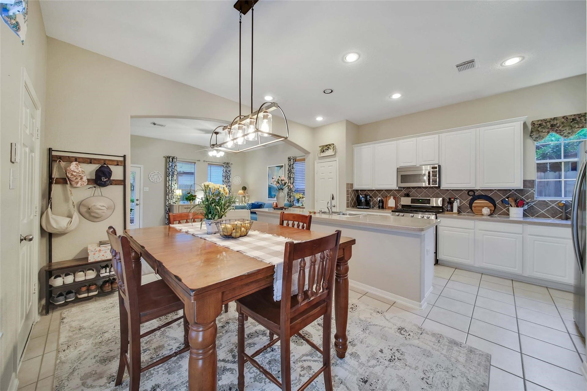This is a spacious, well-lit kitchen with white cabinetry, modern appliances, and a tile backsplash. It features ample counter space and opens up to a dining area, ideal for entertaining.