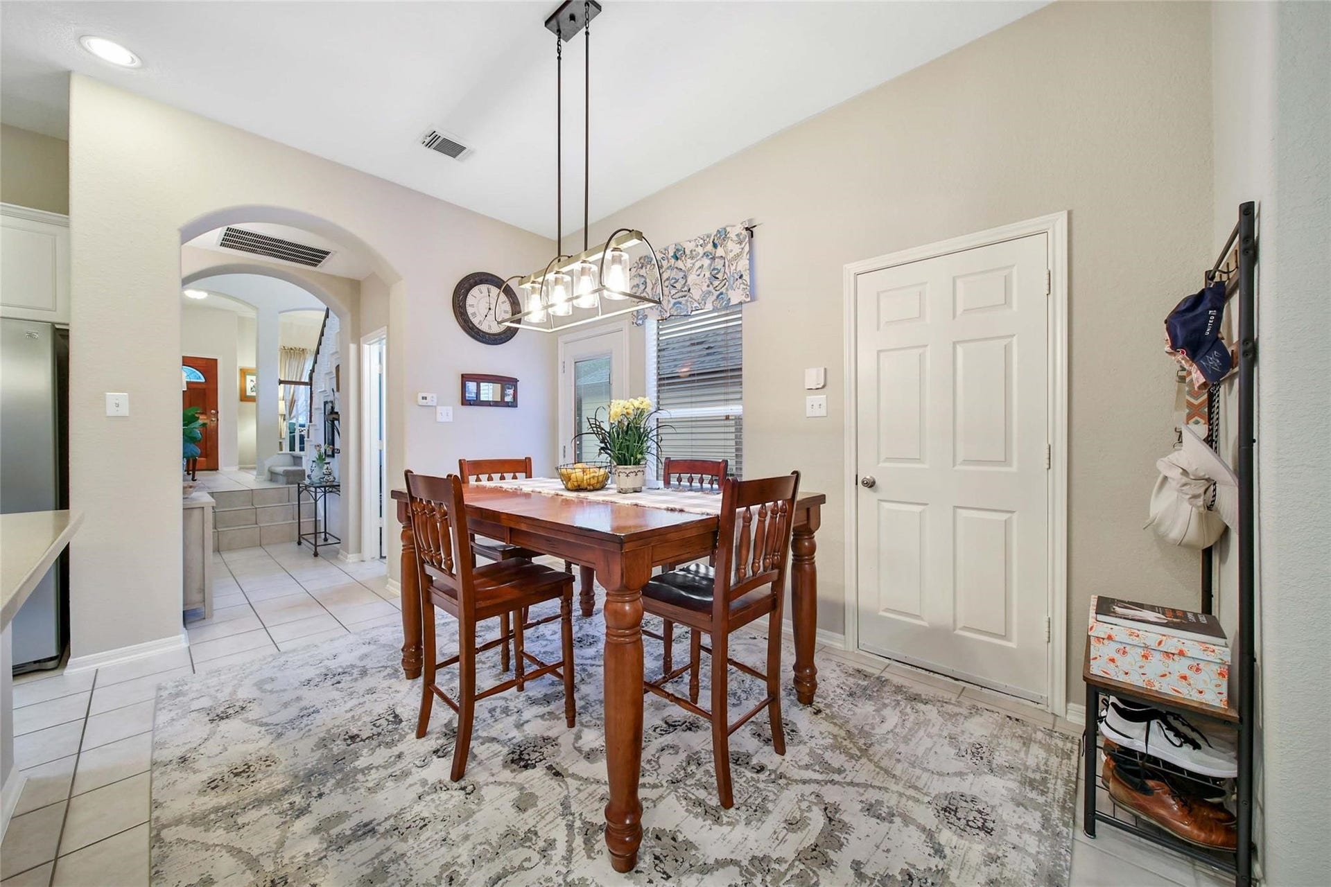 This is a bright, open-concept dining area adjacent to a spacious kitchen with white countertops and cabinetry, complemented by modern appliances. The dining space is well-lit, featuring a stylish chandelier and large windows.