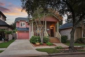 Charming two-story home with a welcoming front porch, attractive pink siding, and an attached garage, nestled in a neighborhood with mature trees and a beautiful sunset sky.