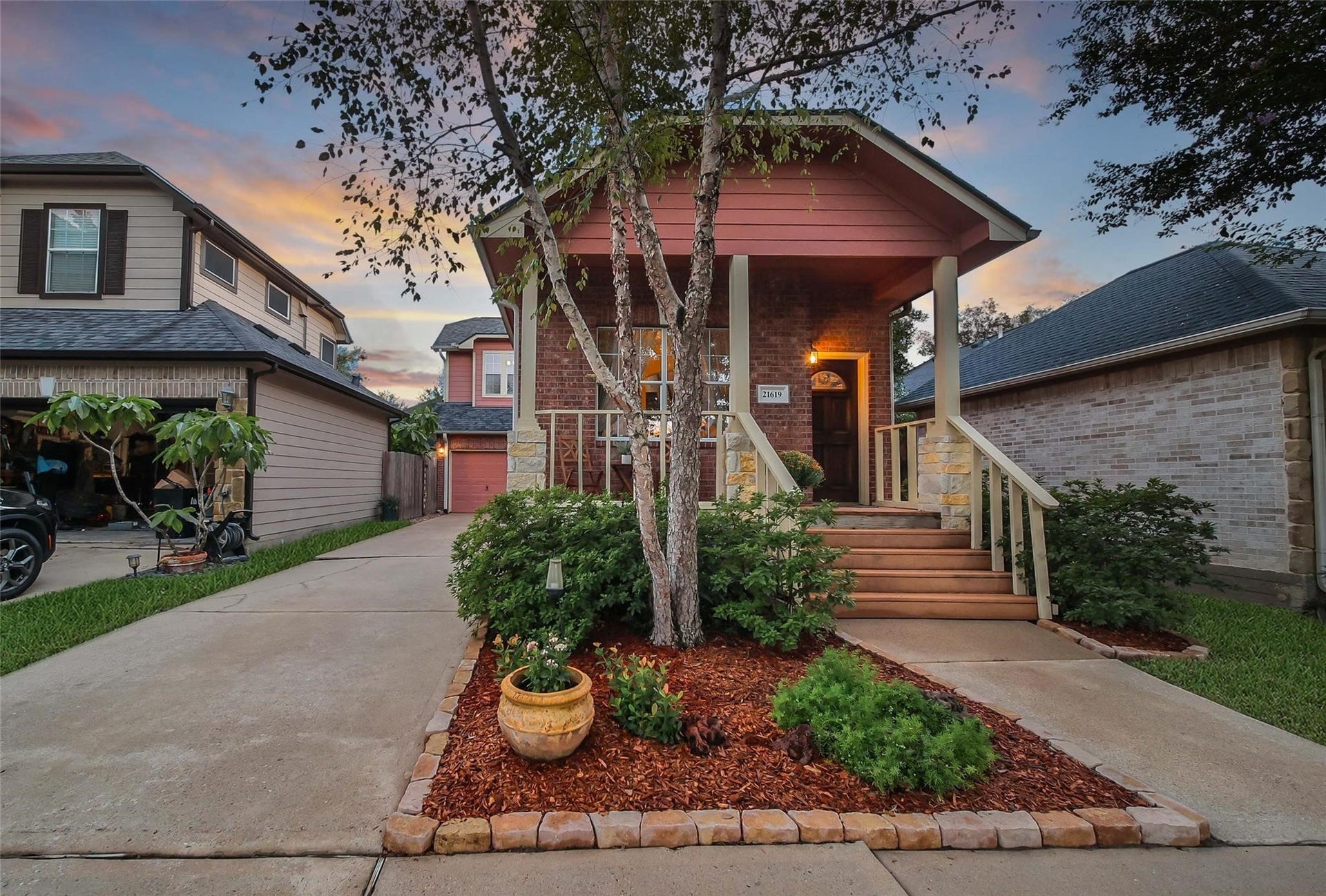 Charming single-family home featuring a welcoming front porch, a well-manicured lawn with mature trees, and an inviting entrance. The property includes a driveway and is located in a pleasant neighborhood with a sunset backdrop.