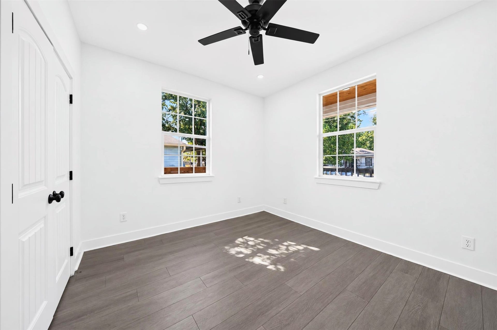 This bedroom features a large windows for ample natural light and a pleasant yard view. Neutral color walls and a ceiling fan contribute to a serene atmosphere.