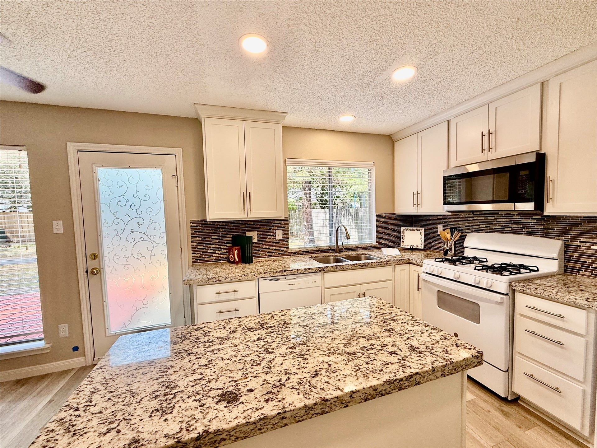 6 Leverwood Court, The Woodlands, TX 77381 Updated kitchen featuring white Shaker-style cabinetry, granite countertops, and a stylish tile backsplash.