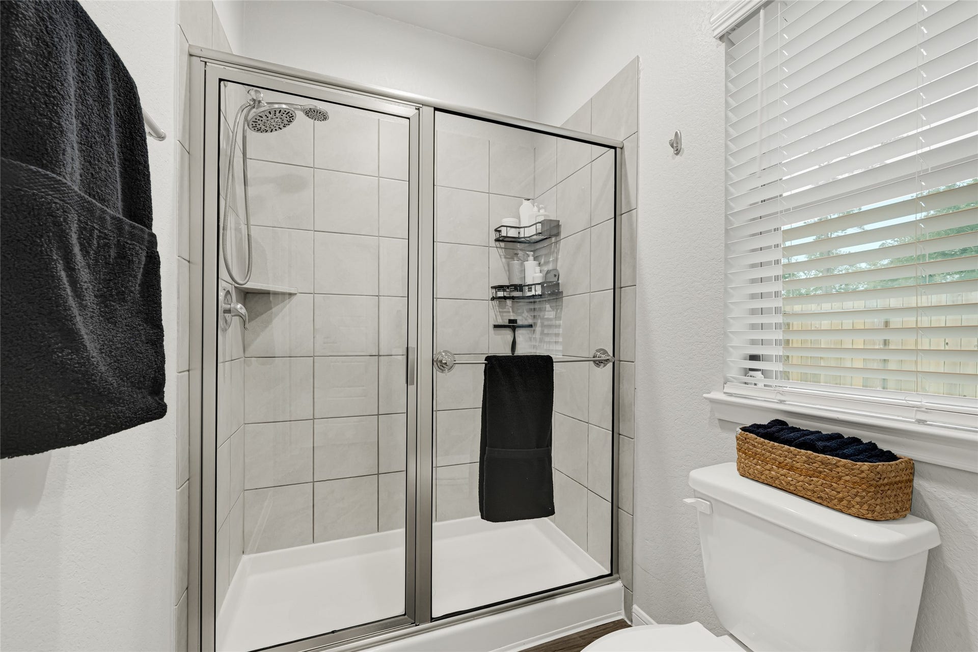 515 Emerald Thicket Lane, Houston, TX 77336 This bathroom features an up graded modern glass-enclosed oversized shower with tiled walls, a window with 2 inch faux wood blinds for natural light, and a neatly organized upgraded elongated commode. This Primary bathroom offers a spacious interior and plenty of room for your storage needs.