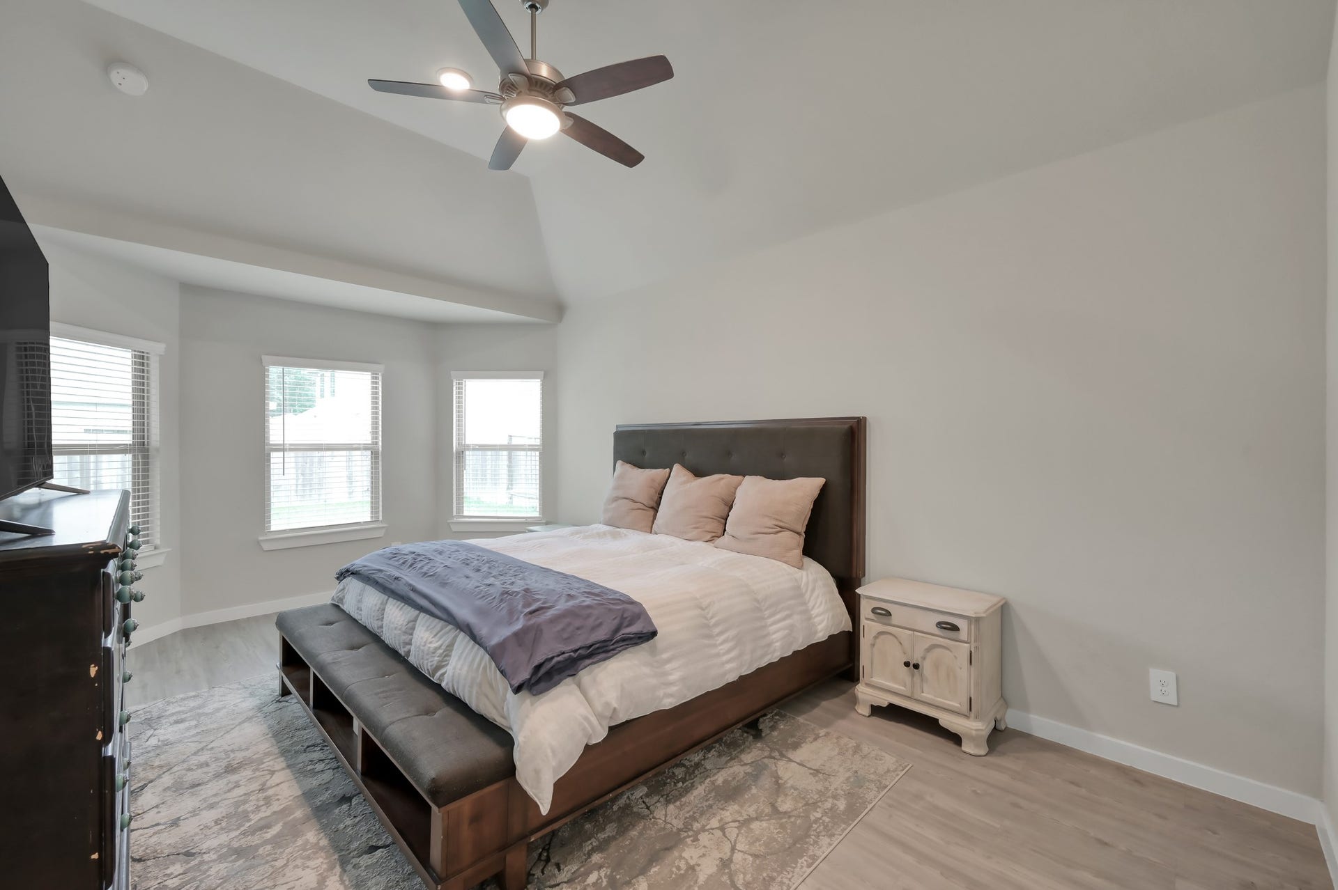 22203 Cardinal Crest Lane, New Caney, TX 77357 This bedroom features a cozy setup with a large bed, a ceiling fan, and ample natural light from multiple windows. It has a neutral color palette and includes a nightstand and dresser, creating a comfortable and inviting space.