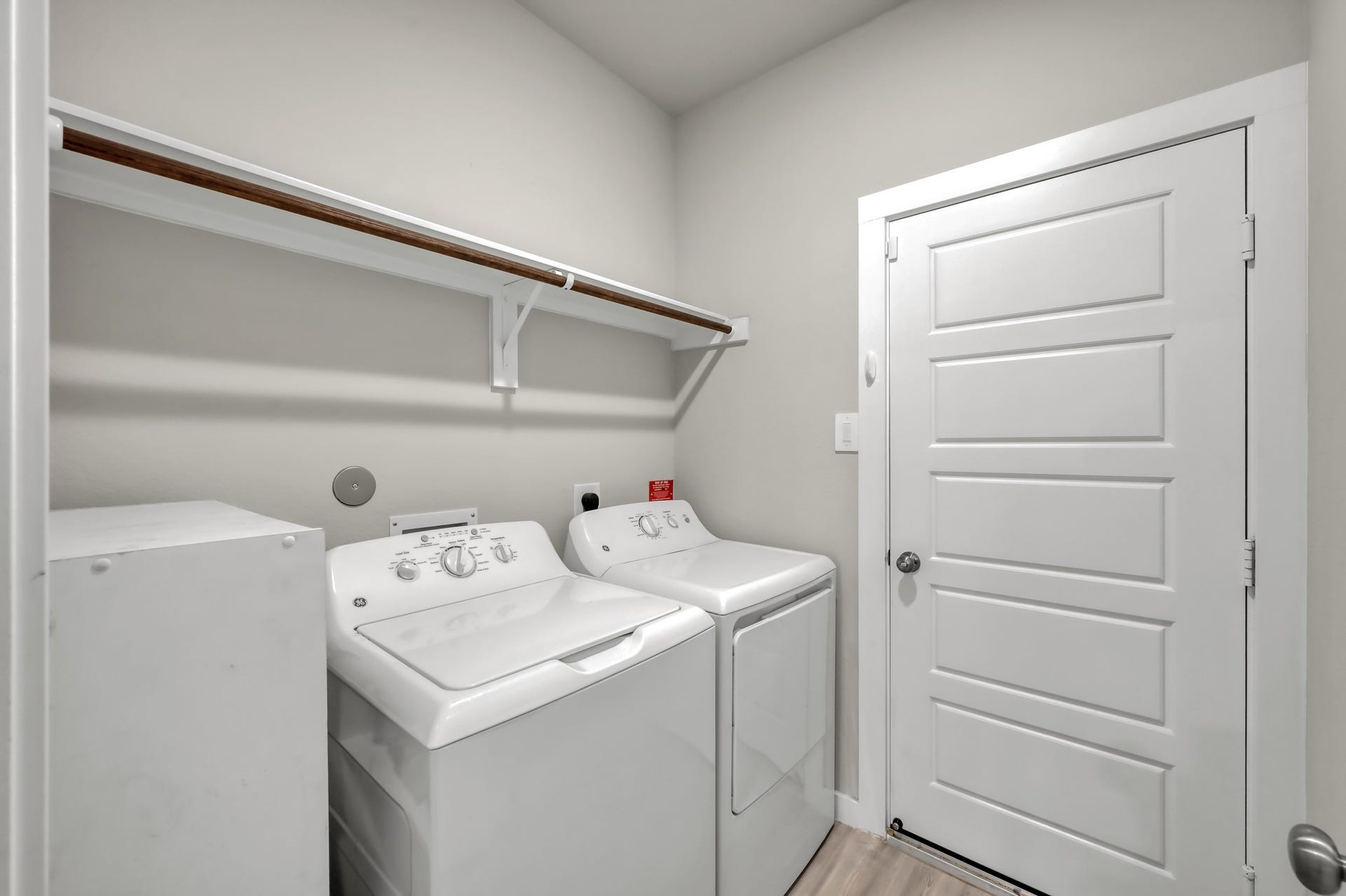 22203 Cardinal Crest Lane, New Caney, TX 77357 Compact laundry room with washer and dryer, featuring a shelf for storage and a white door. Neutral wall color and light wood flooring create a clean, functional space.